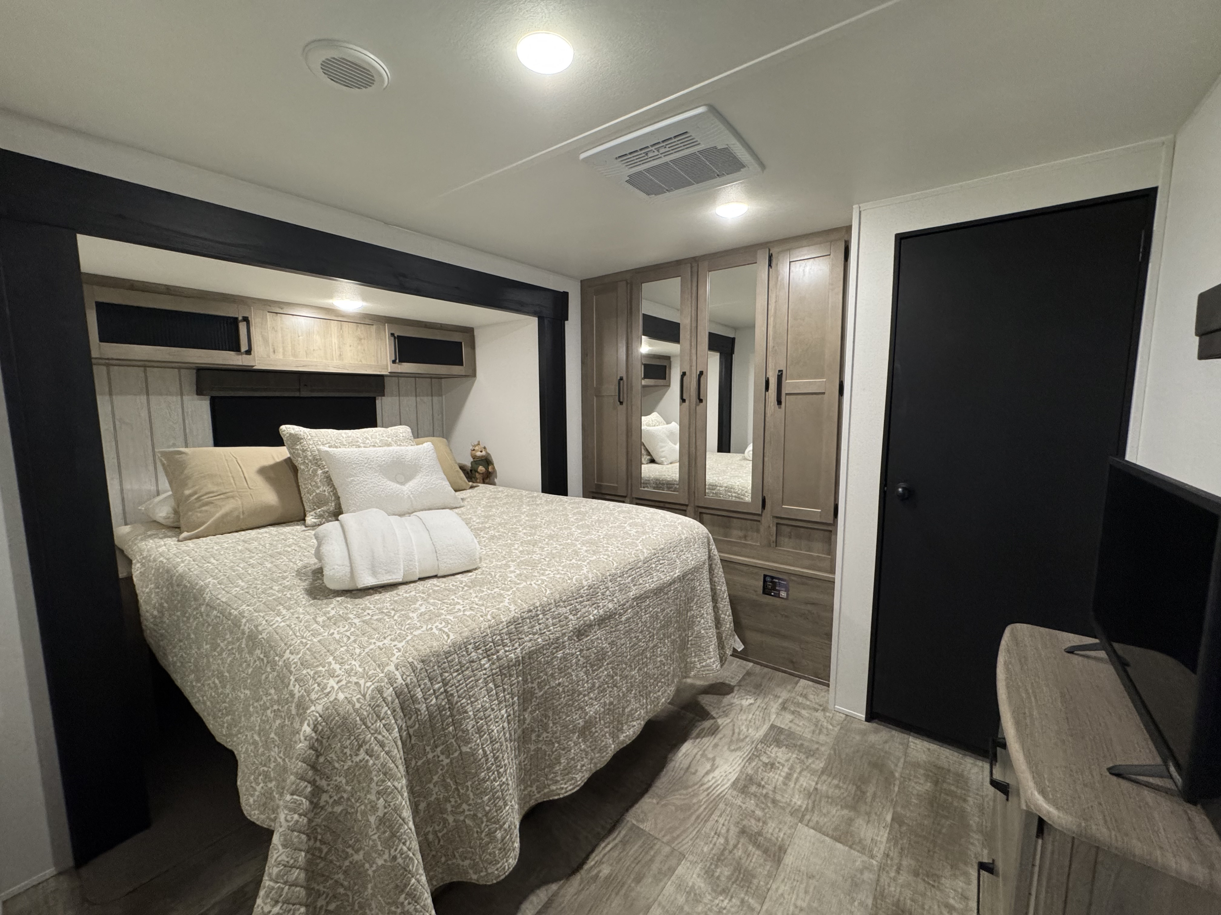 Inviting RV rental bedroom with a comfortable bed, mirrored closet, overhead storage, light wood cabinetry, and modern flooring.. forest river Puma 2025