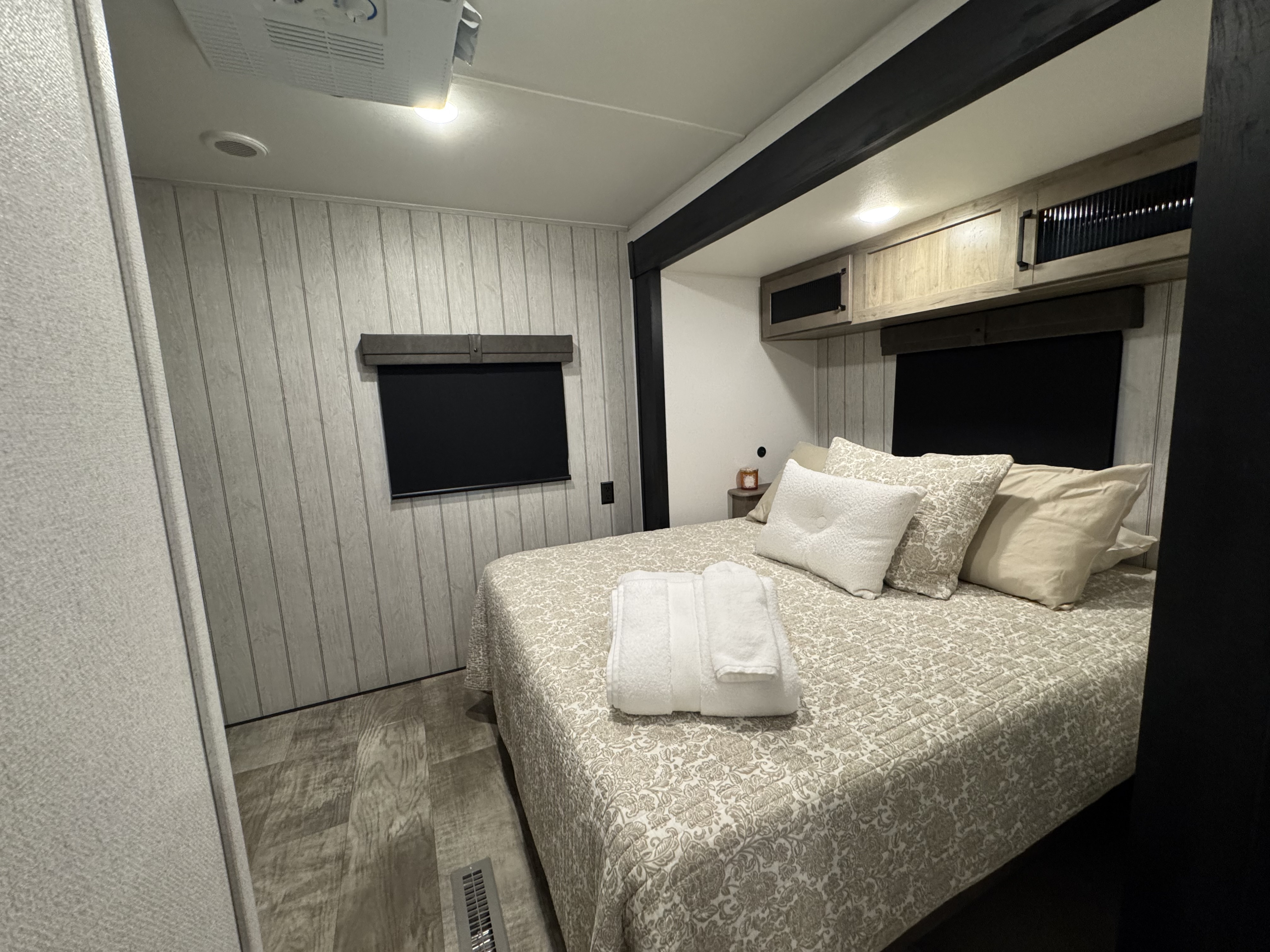 Cozy RV rental bedroom with a patterned quilt on the bed, folded towels, light wood-paneled walls, and a window blind.. forest river Puma 2025