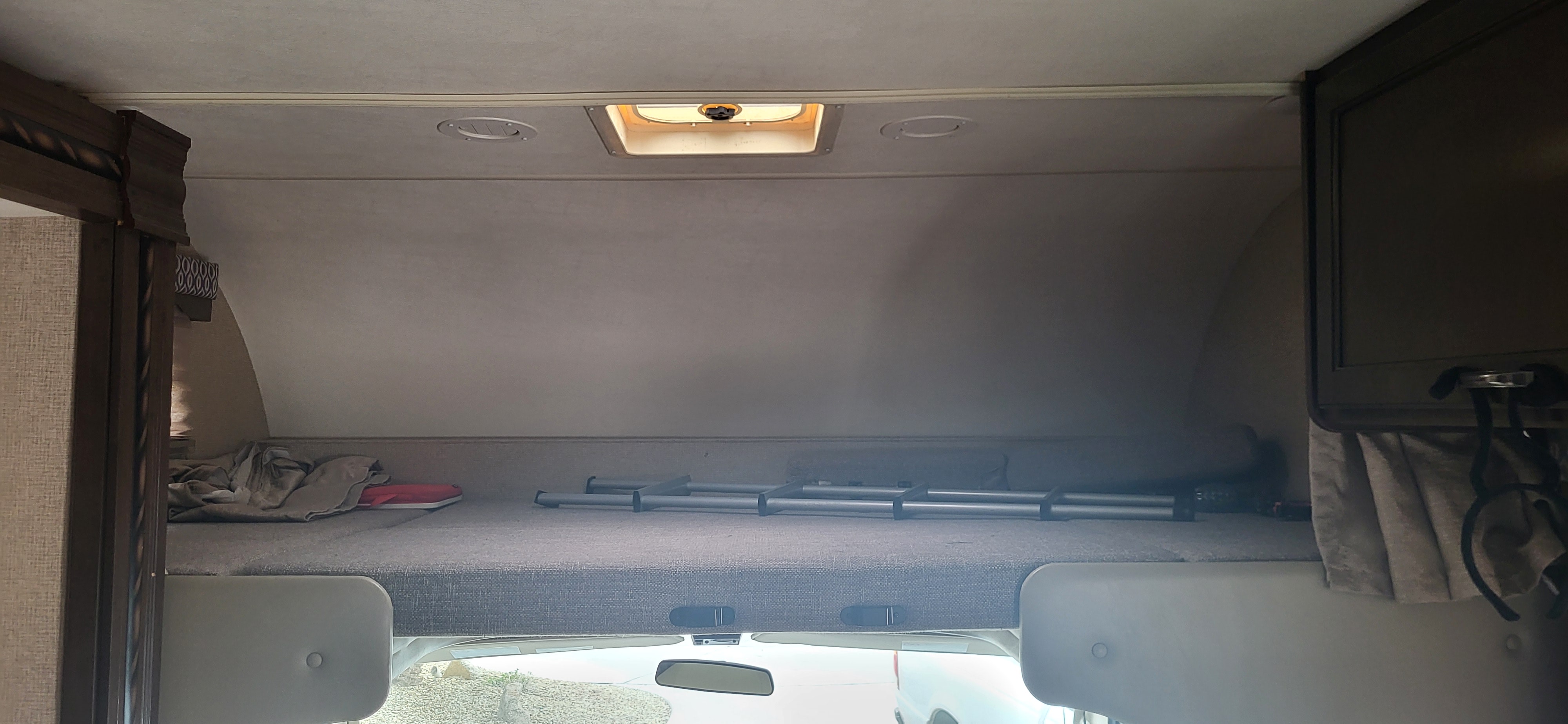 Interior view of an RV rental: a large overhead bunk bed above the cab, featuring a mattress, folded bedding, and a collapsible ladder. Ideal extra sleeping space.. Thor Freedom Elite 2017