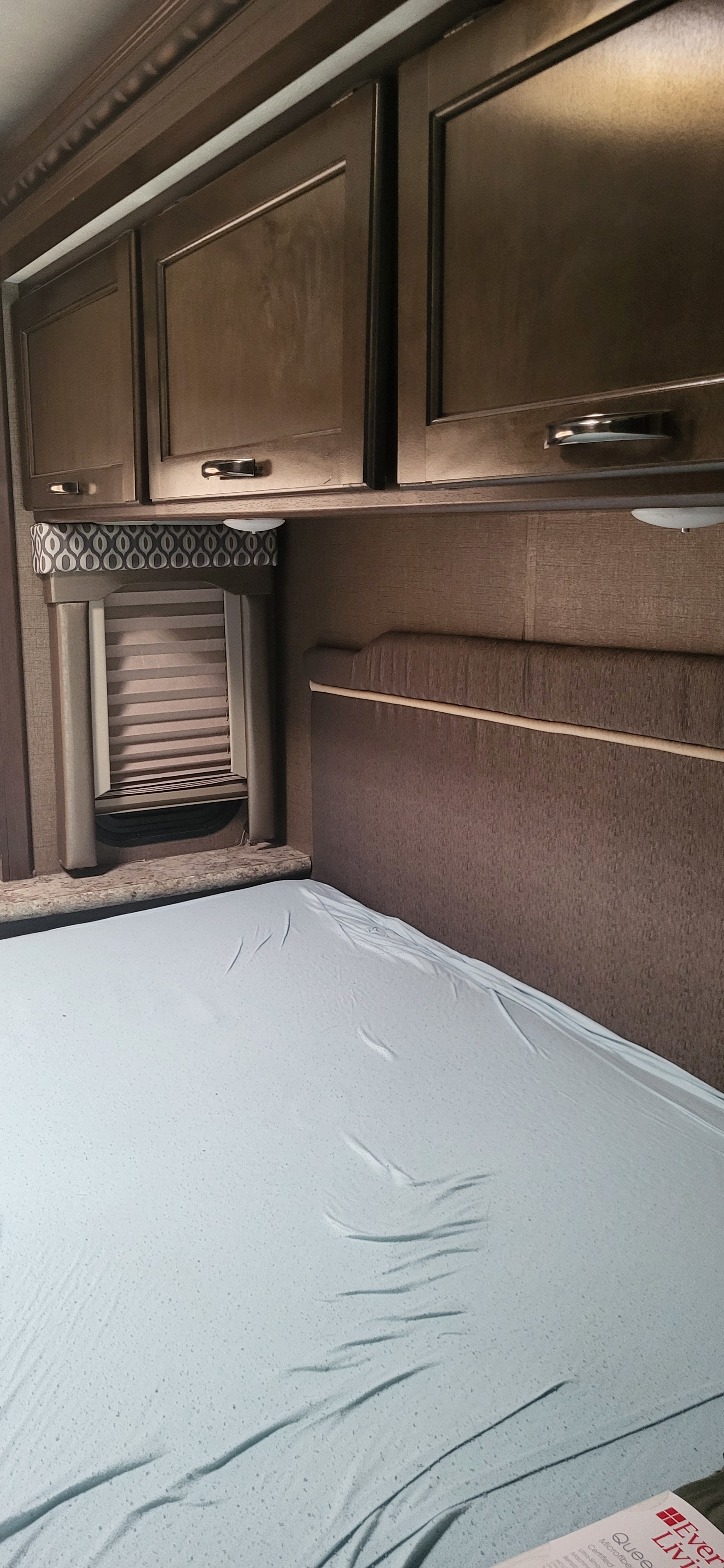 **RV rental** bedroom interior featuring overhead cabinets, a window with blinds, and a bed with a light blue fitted sheet.. Thor Freedom Elite 2017