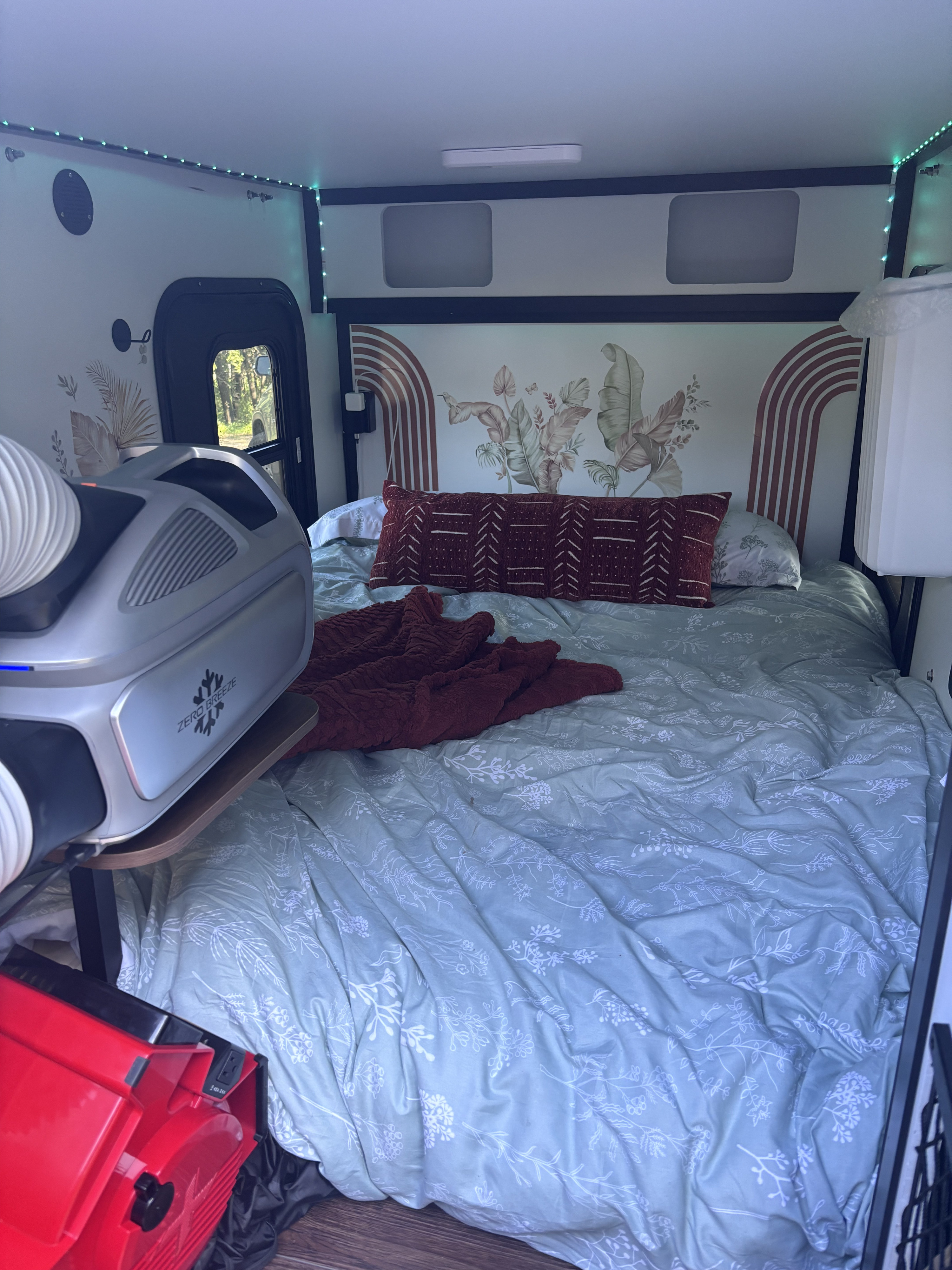 Cozy RV rental interior featuring a bed with botanical decor, LED lighting, and a portable Zero Breeze AC unit for comfort.. Tiny Camper Company 5X8 CUBE OFF ROAD 2025