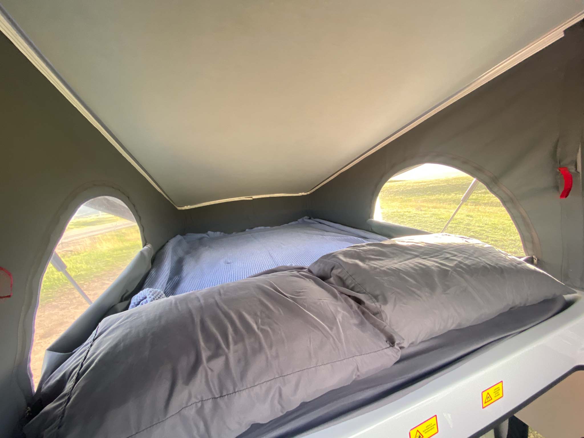 Cozy pop-top rv rental sleeping area with bedding, pillows, and outside views of a grassy field through side windows.. Winnebago Solis 2022