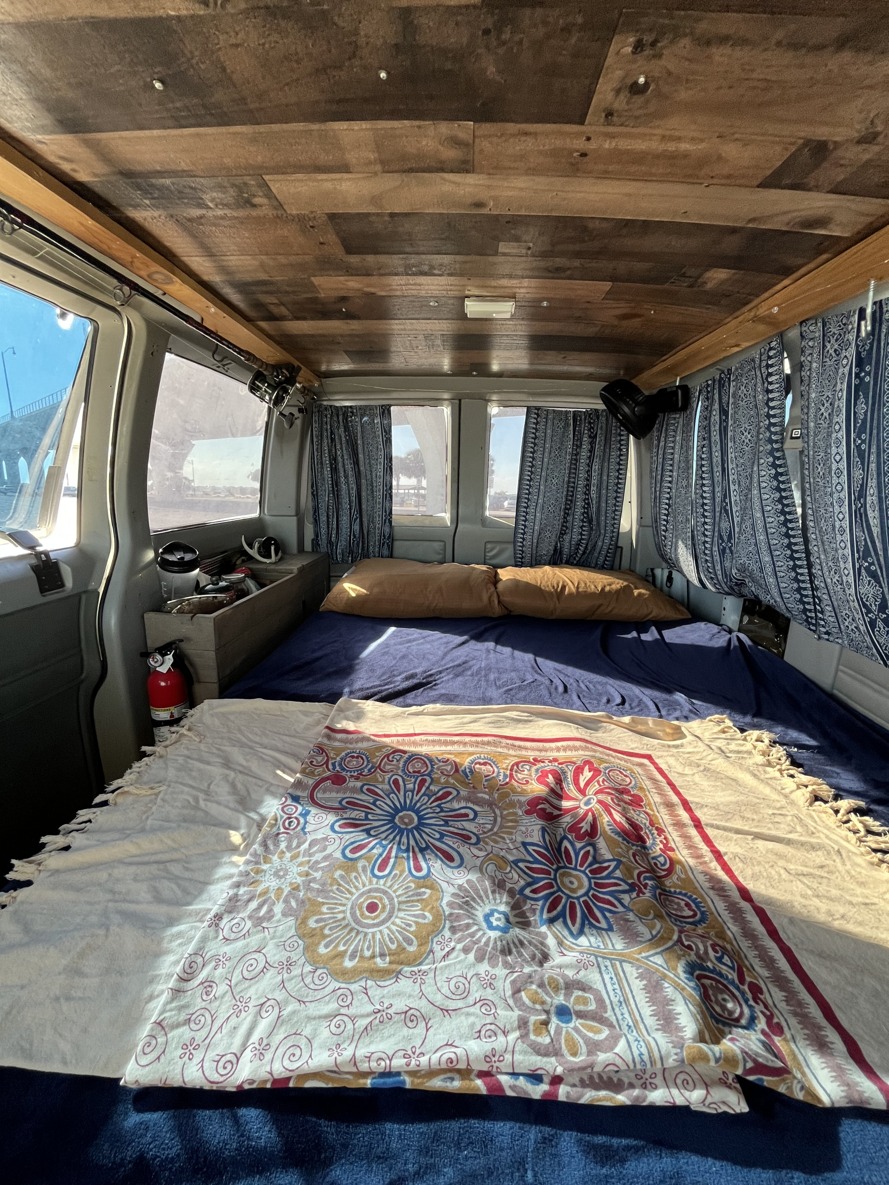 Cozy rv rental van interior with bed, wood ceiling, patterned curtains, fire extinguisher, and fishing rods for adventure.. Chevrolet Astro 1992