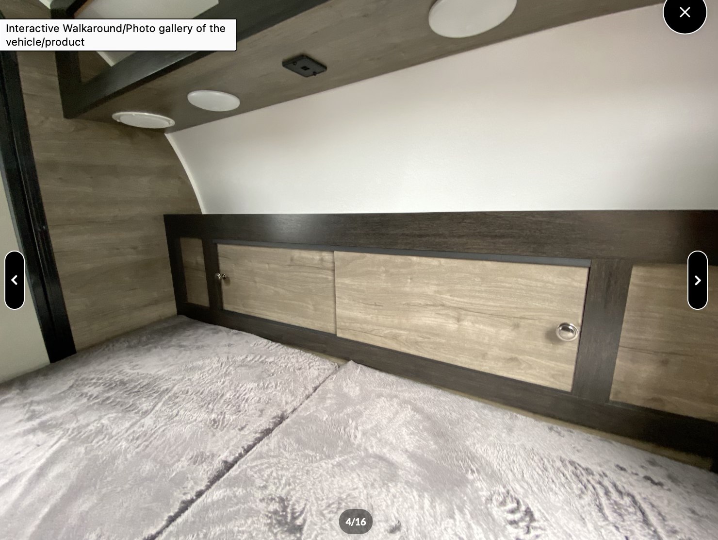 Cozy RV rental bedroom showing a bed with a grey blanket, wooden headboard storage cabinets, and overhead lighting.. Braxton Creek Bushwhacker 2022