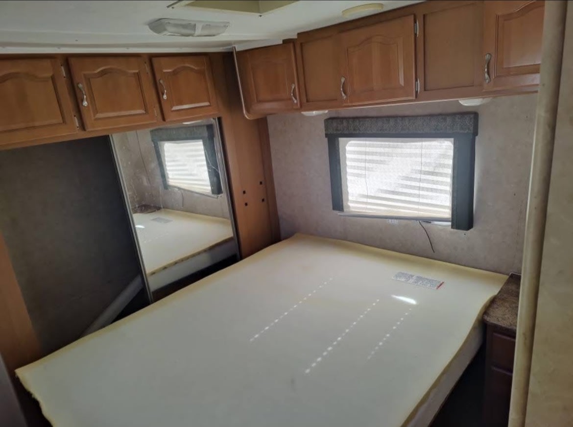 RV rental bedroom: A bed, wood cabinets, window with blinds, and a large mirror create a compact sleeping space.. Gulf Stream Conquest 2007
