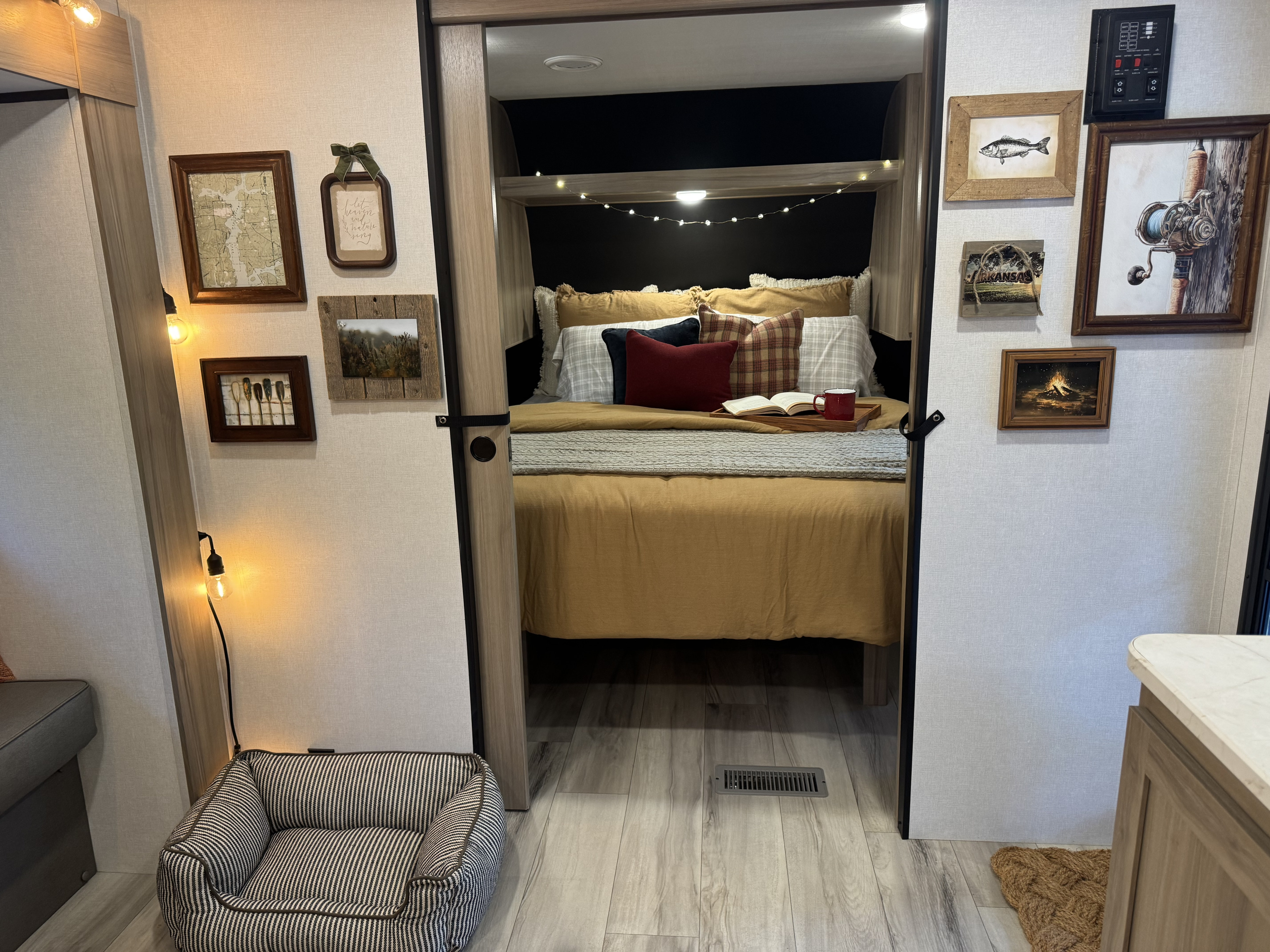 Cozy RV rental bedroom nook with warm string lights, framed nature art, and a striped pet bed.. Keystone RV Coleman 2025