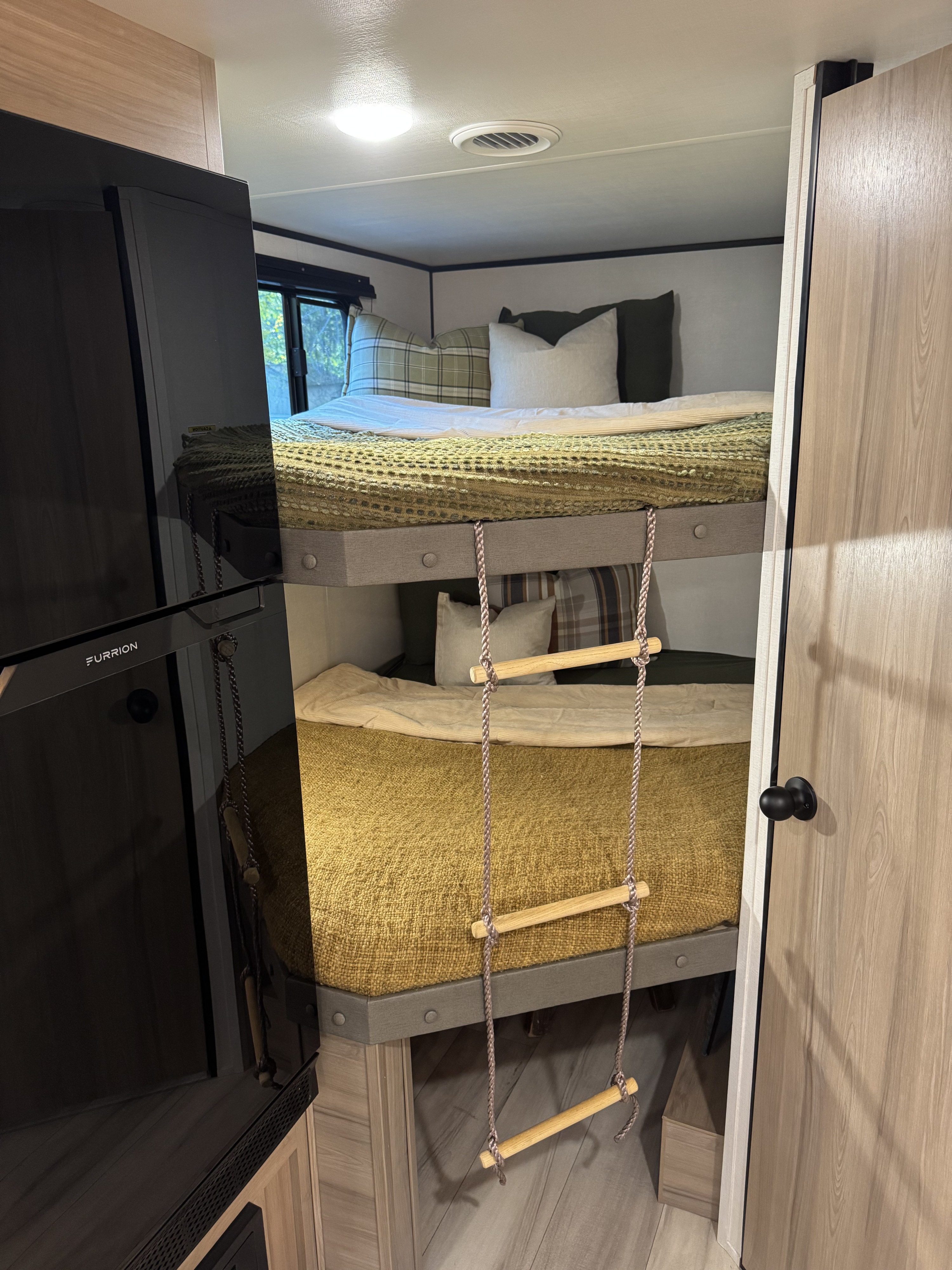 Cozy RV rental bunk beds feature a fun rope ladder and plush green/beige bedding, ideal for family travel.. Keystone RV Coleman 2025