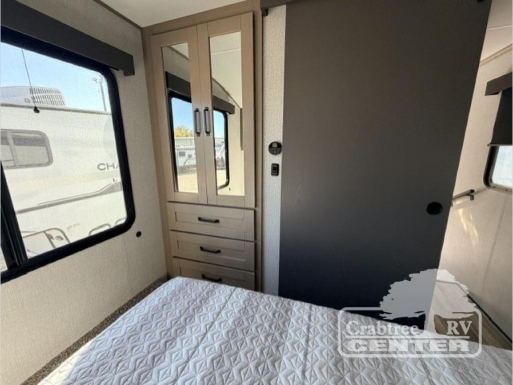 This RV rental bedroom features a cozy bed, large window, mirrored wardrobe storage with drawers, and a dark sliding door.. Grand Design Reflection 150 2025