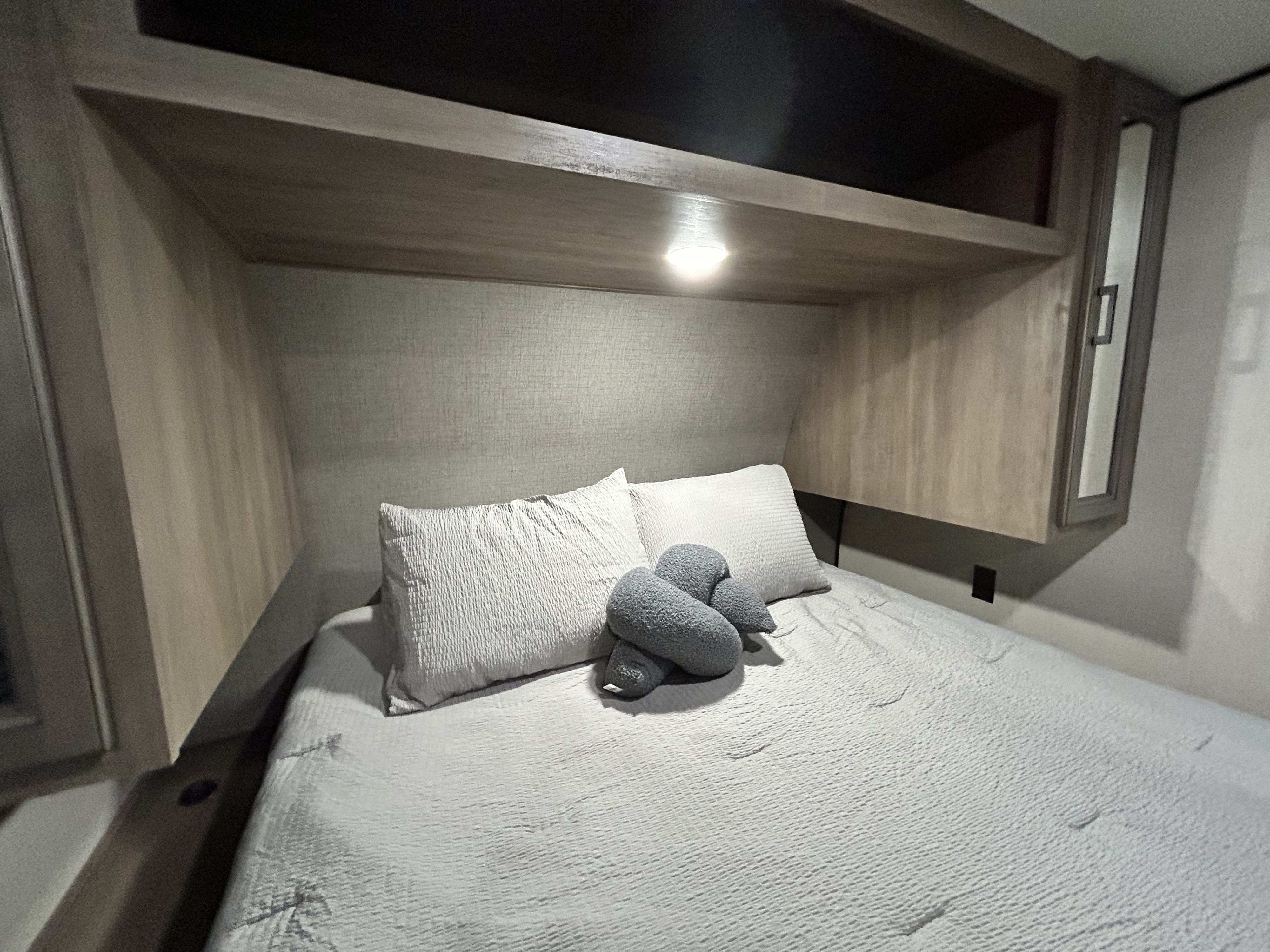 Cozy RV rental bedroom featuring a comfortable bed, soft pillows, and overhead storage with an illuminated light.. Highland Ridge RV BHS26 2023