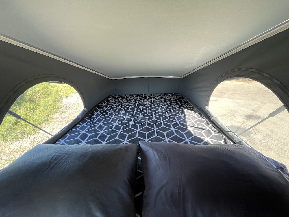 Cozy pop-top bed inside an RV rental, offering comfortable sleeping with scenic views through arched windows.. Dodge Winnebago 2021