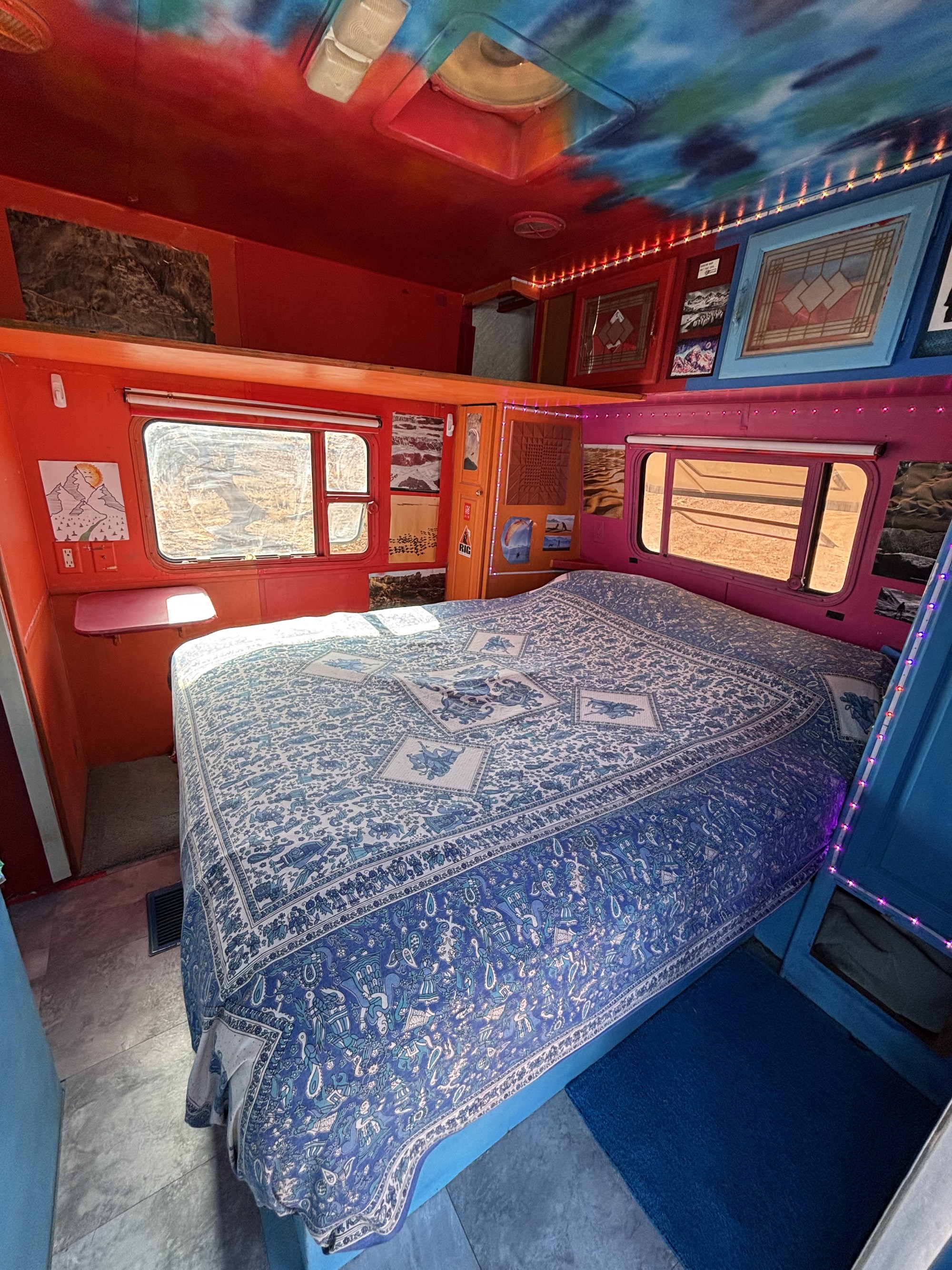 Vibrant rv rental interior: A cozy bedroom with a patterned bedspread, red walls, and tie-dye ceiling.. Warn The West TumbleWeed 2026