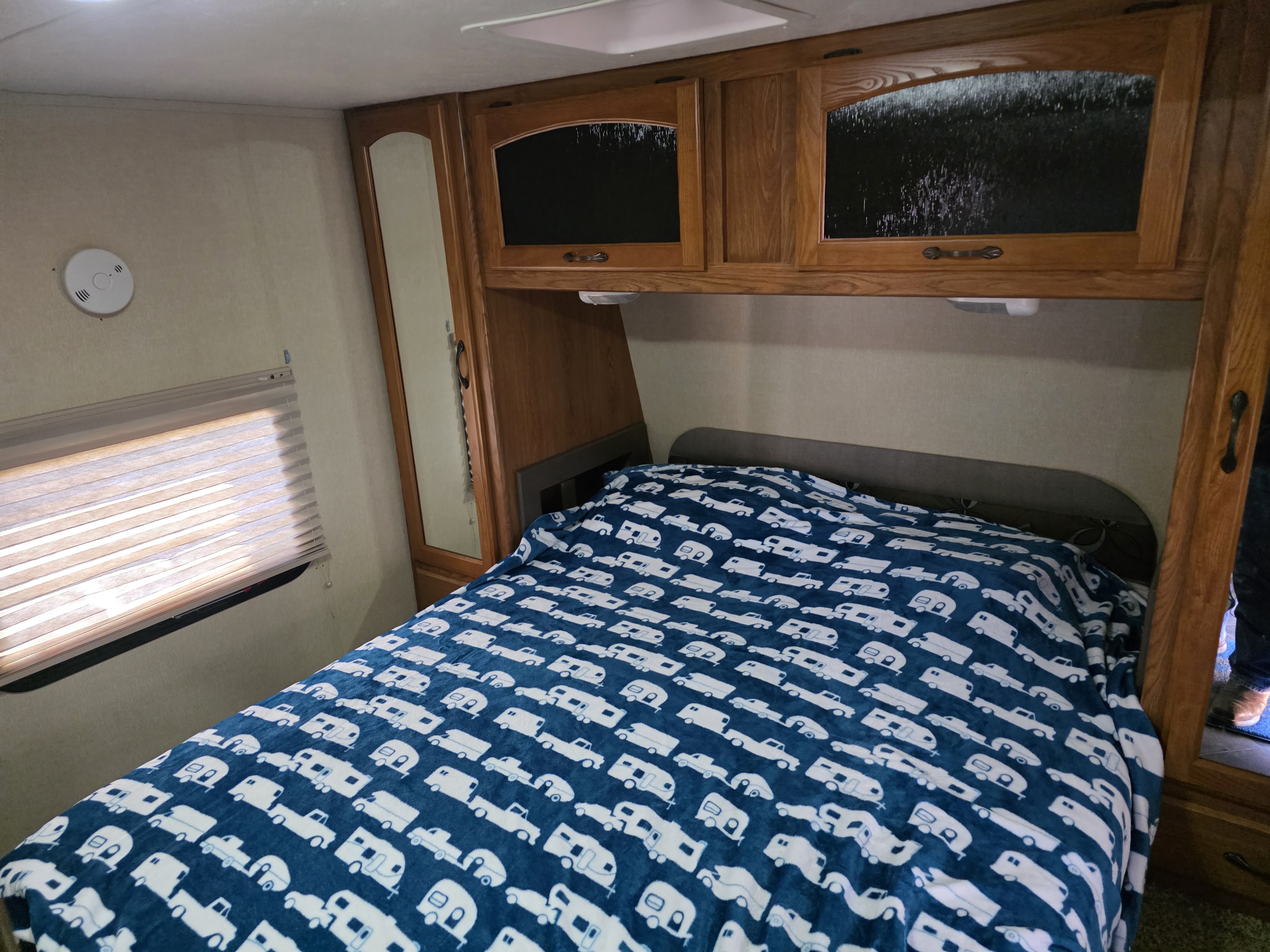 Check out this cozy RV rental bedroom, featuring a bed with a camper blanket, wooden cabinets, and a window.. Keystone RV Sprinter 2013