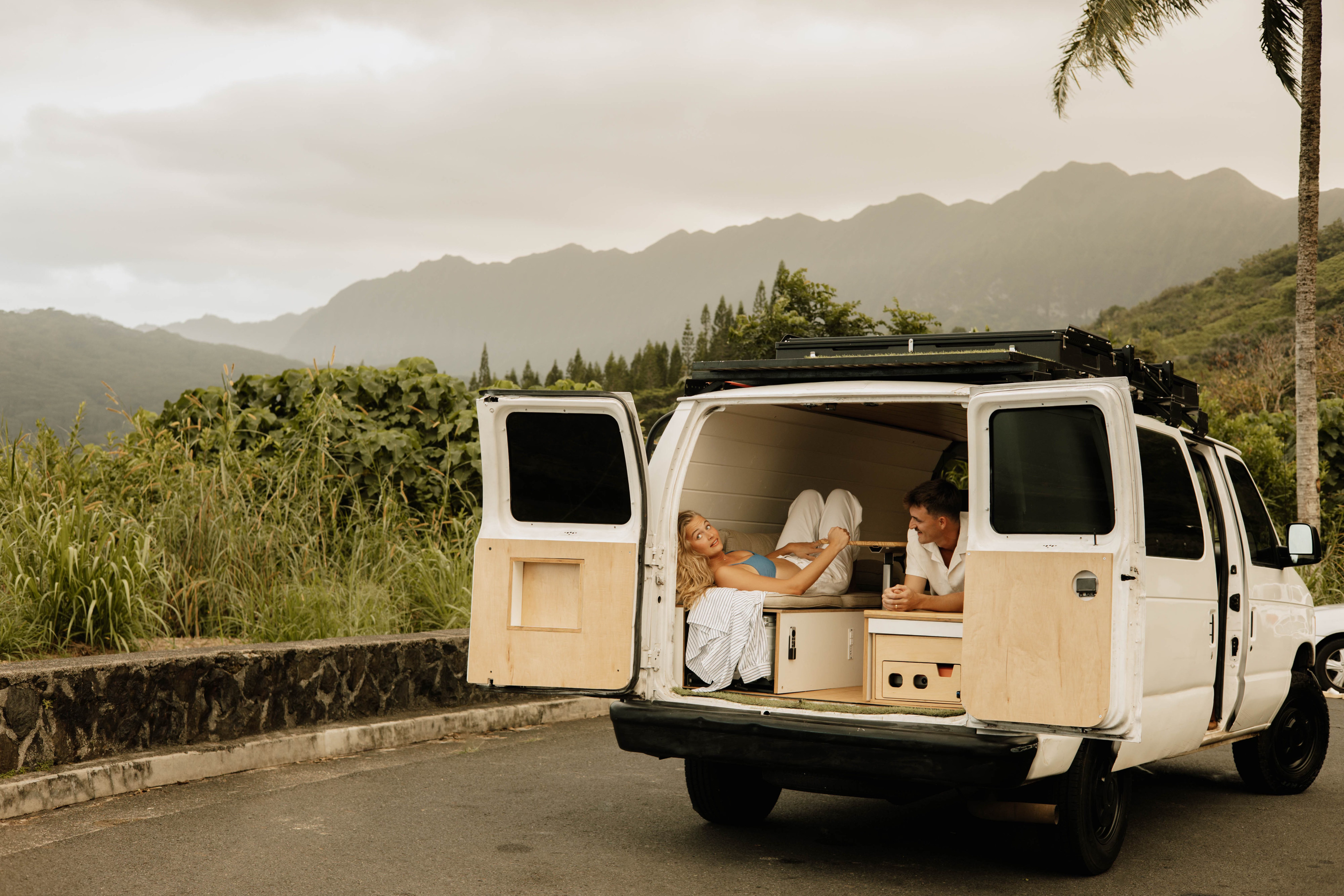 Couple relaxing in their RV rental campervan, parked with scenic mountain views. Perfect for van life adventures!. Ford Econolline 250s 2005