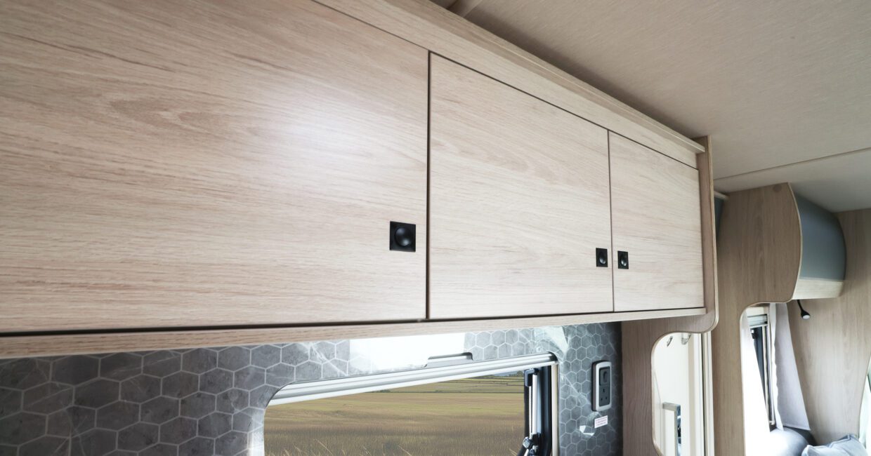 Overhead light wood cabinets with black latches in a modern RV rental. Hexagonal backsplash and window view add style.. Auto Trail Expedition C73 - 2026 2026