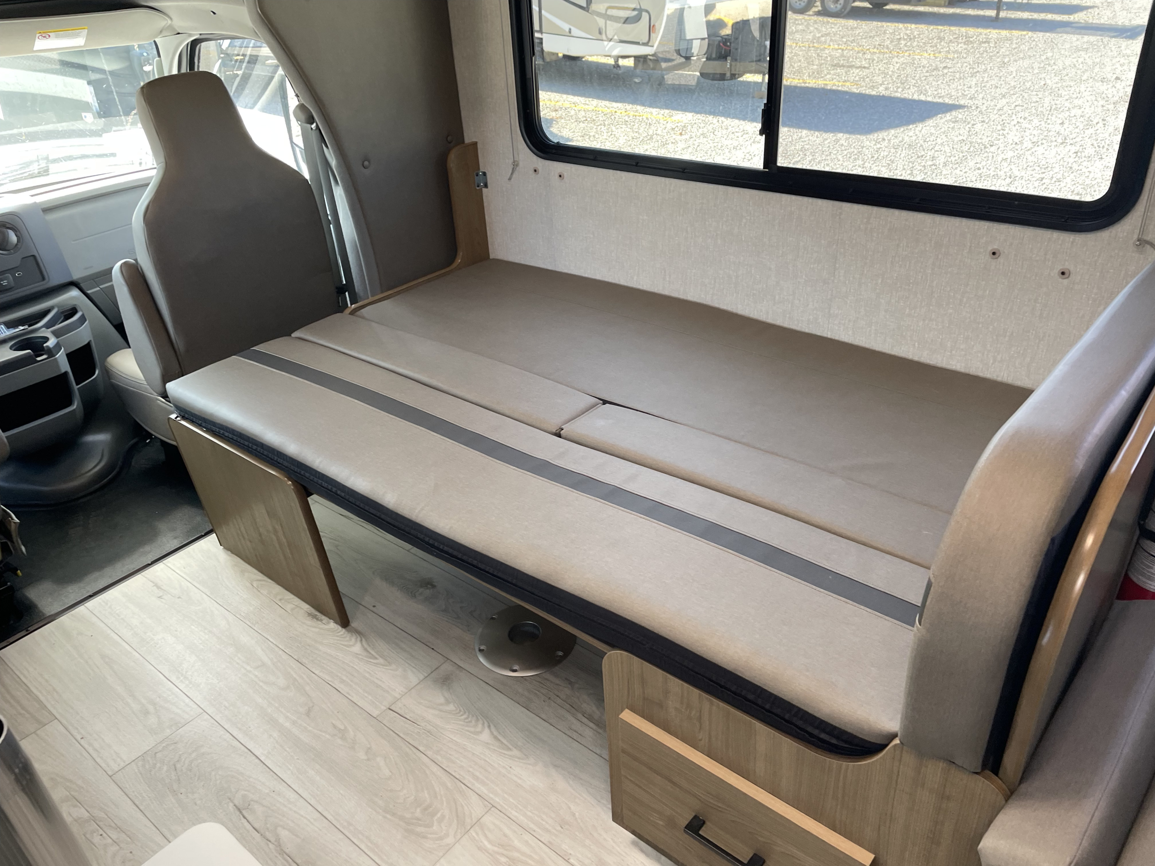 RV rental interior showing a convertible dinette bed with light cushions and wooden supports next to a window.. Forest River Coachmen Leprechaun 2025