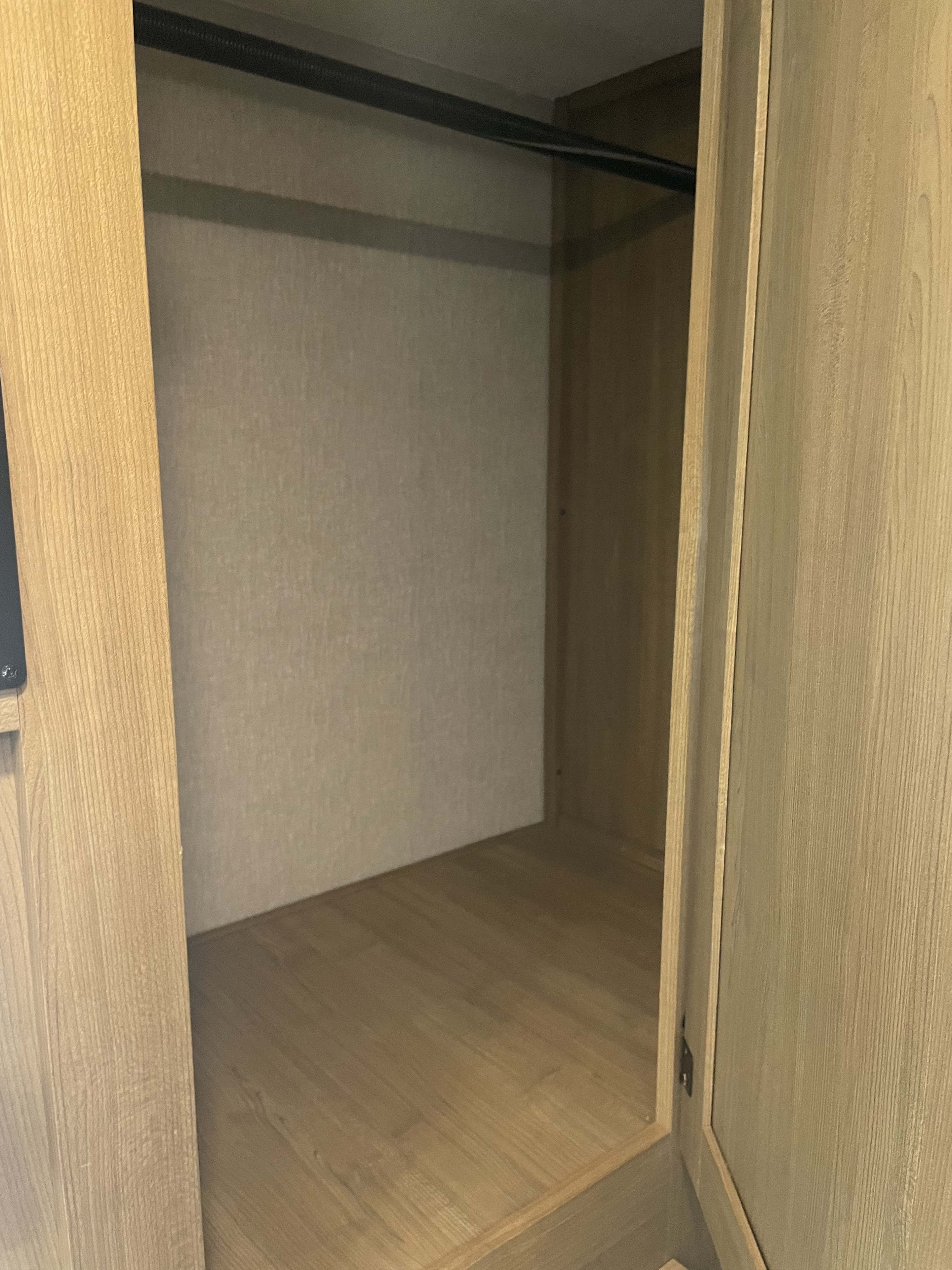 Empty RV rental closet with a metal hanging rod and light wood interior, ready for storage.. Forest River Coachmen Leprechaun 2025