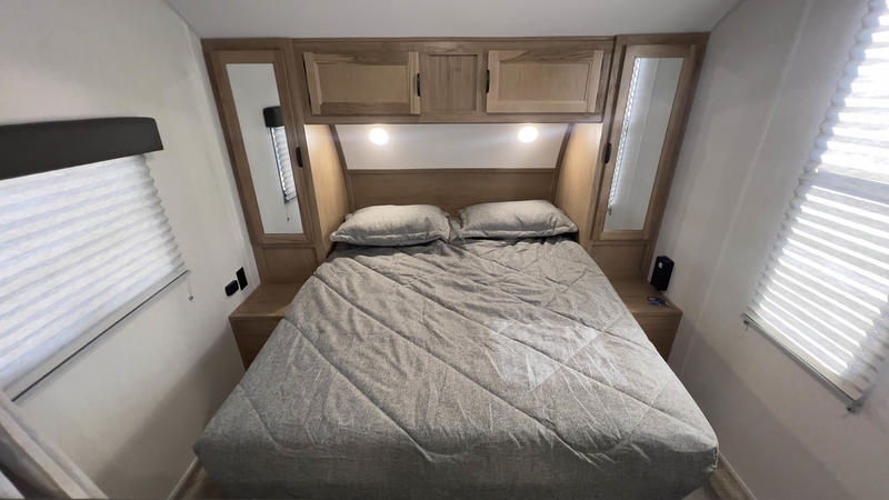 Comfortable RV rental bedroom featuring a queen bed, wood cabinets, reading lights, and window blinds. Ideal for your travel trailer getaway.. Forest River 26' Bunkhouse 2026