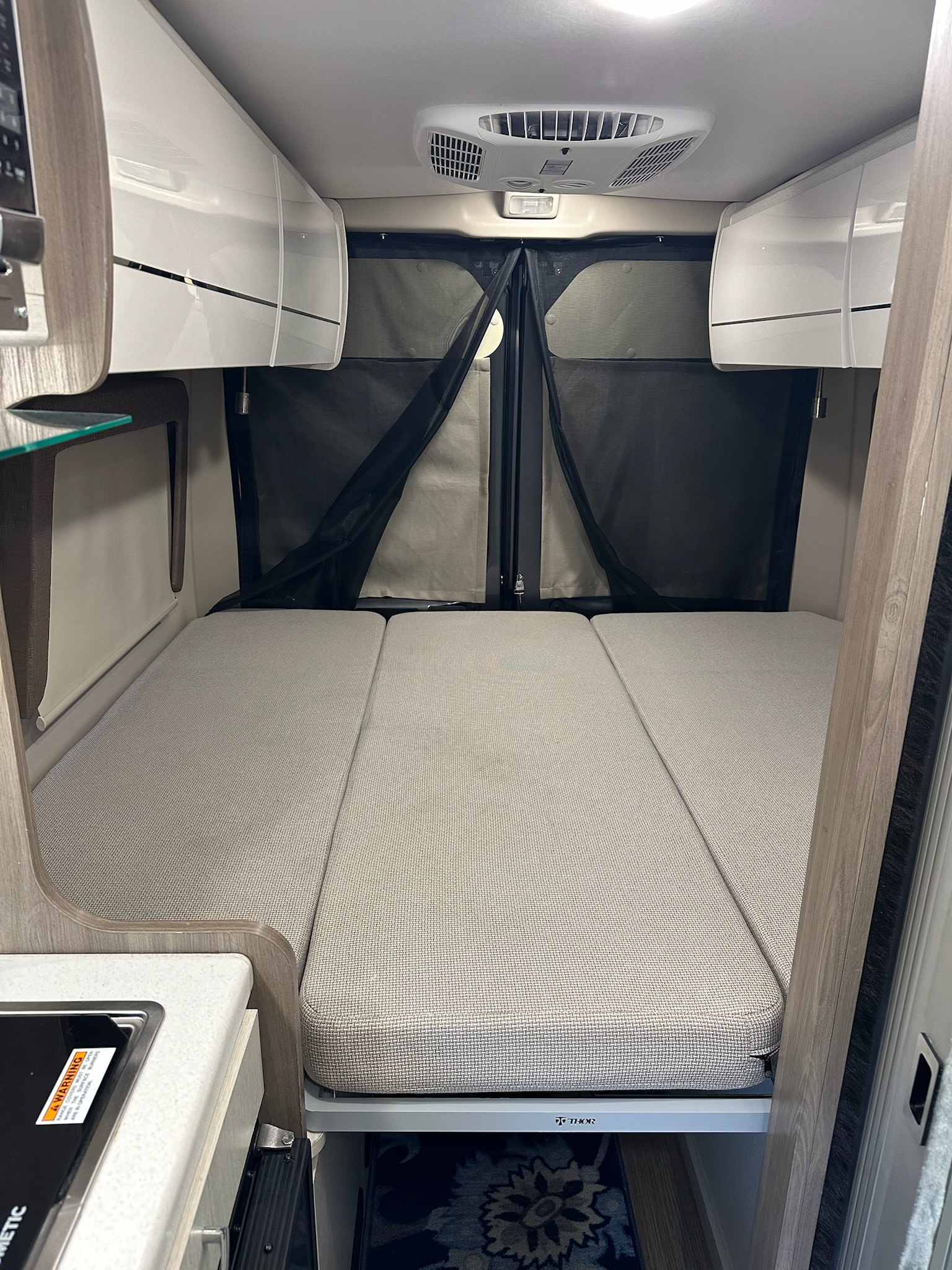 RV rental: Camper van's cozy interior features a bed, overhead storage, and kitchenette for comfortable journeys.. Thor Tellaro 2022