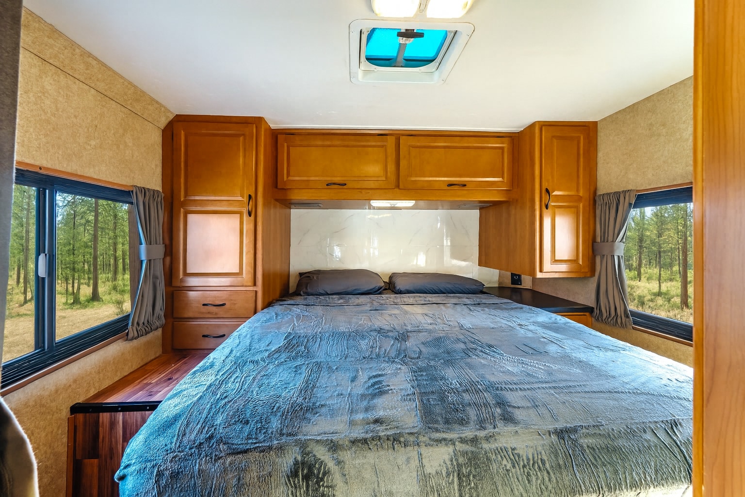 Spacious RV rental bedroom with a large bed, wooden cabinetry, skylight, and stunning forest views from the windows.. Thor Majestic 2017
