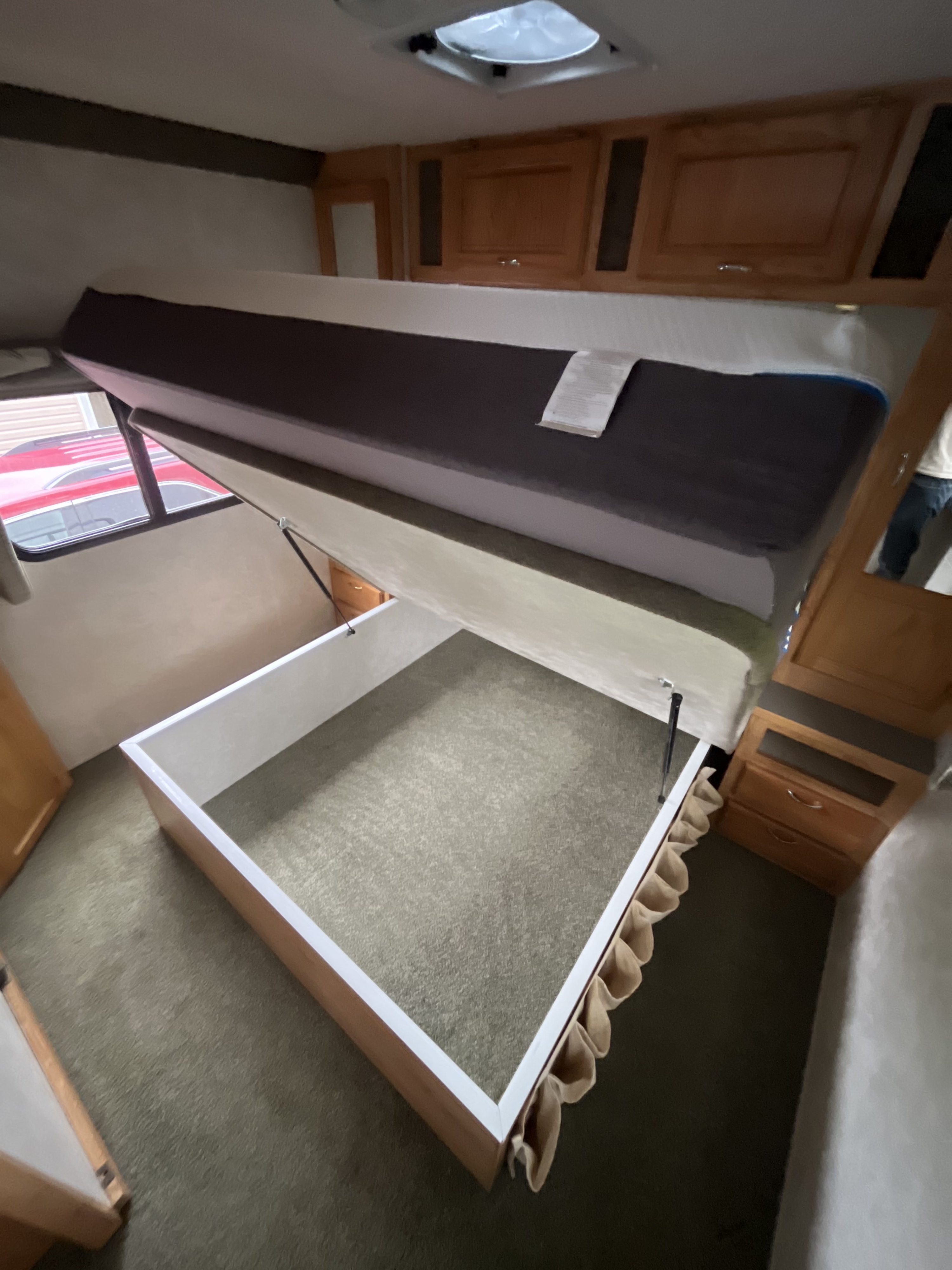 Discover this RV rental's smart bed lift storage. The mattress is raised, revealing a deep, carpeted compartment for travel gear.. Bigfoot RV Bigfoot RV Motorhome 2004