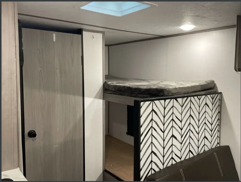 RV rental interior with cozy bunk beds, a closed door, and a ceiling skylight overhead. Ideal for family adventures.. Dutchmen Coleman Lantern LT 2023