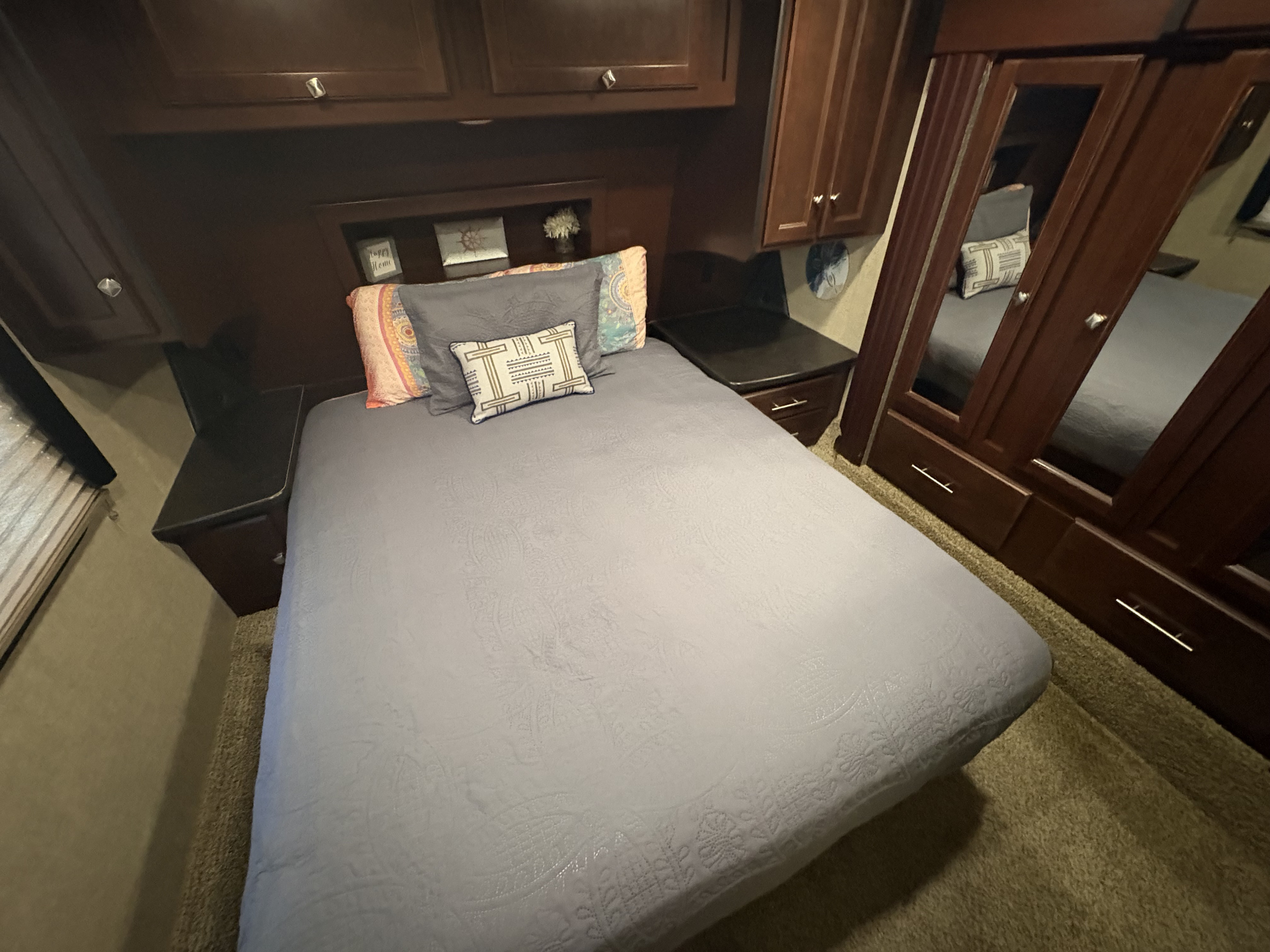 Cozy RV rental bedroom with dark wood storage, a comfy bed, decorative pillows, and a mirrored wardrobe.. Heartland RVs Road Warrior Toy Hauler 2015