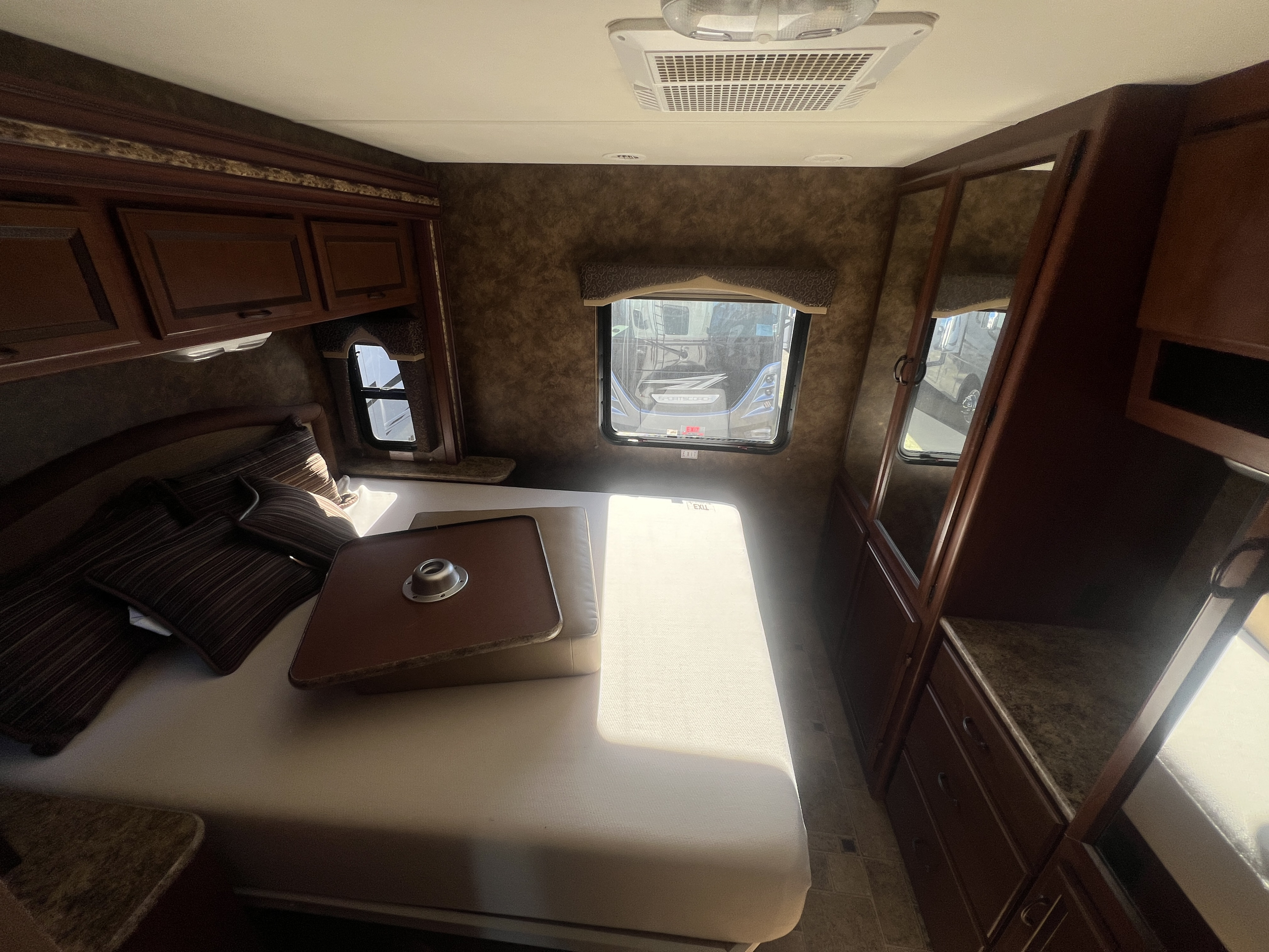 Cozy RV rental bedroom with dark wood cabinets, windows, a comfy bed, and ceiling AC.. Thor Hurricane 2014