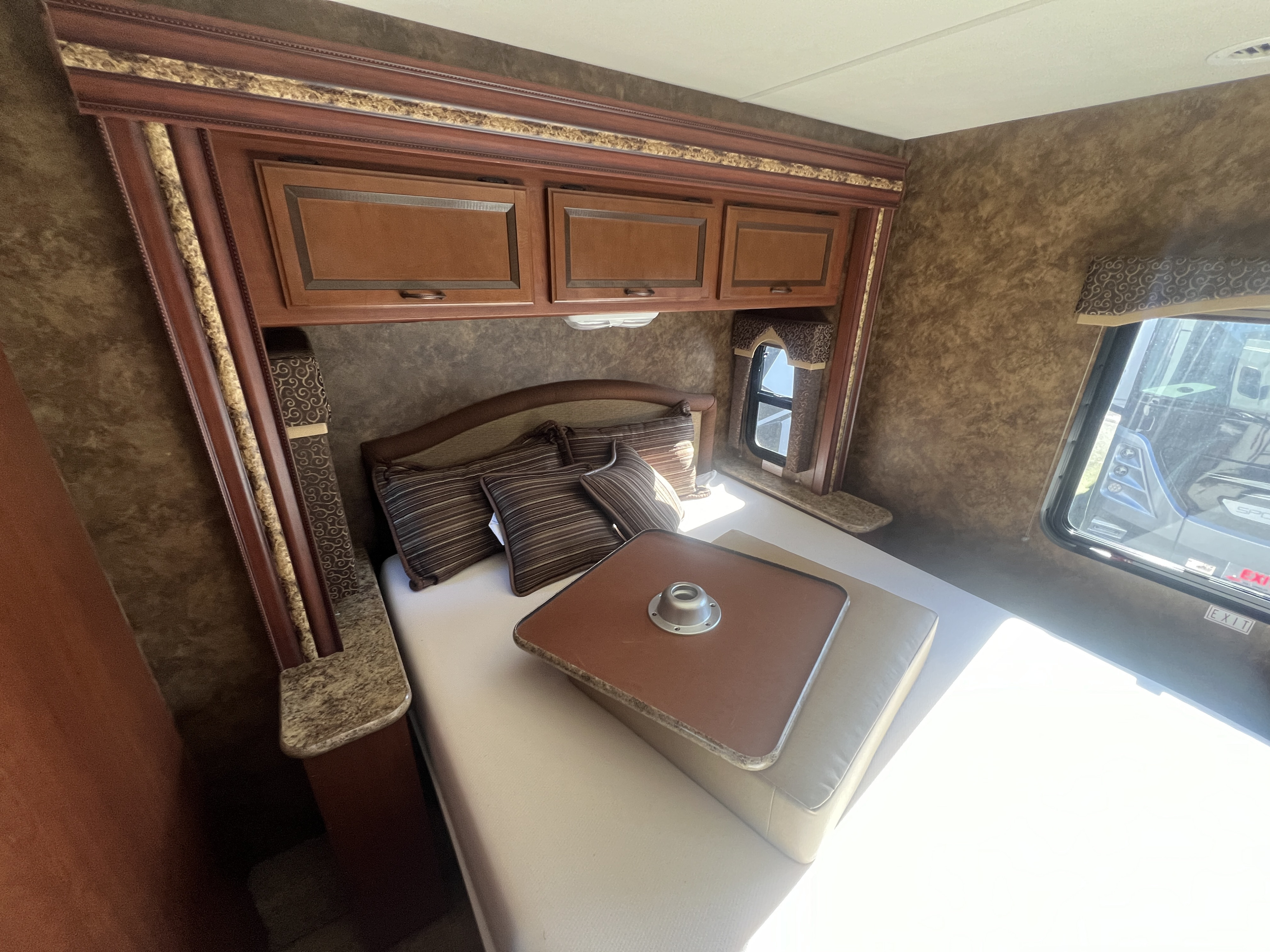 Inviting RV rental bedroom with a comfy bed, overhead storage, side table, window, and a removable bed table.. Thor Hurricane 2014