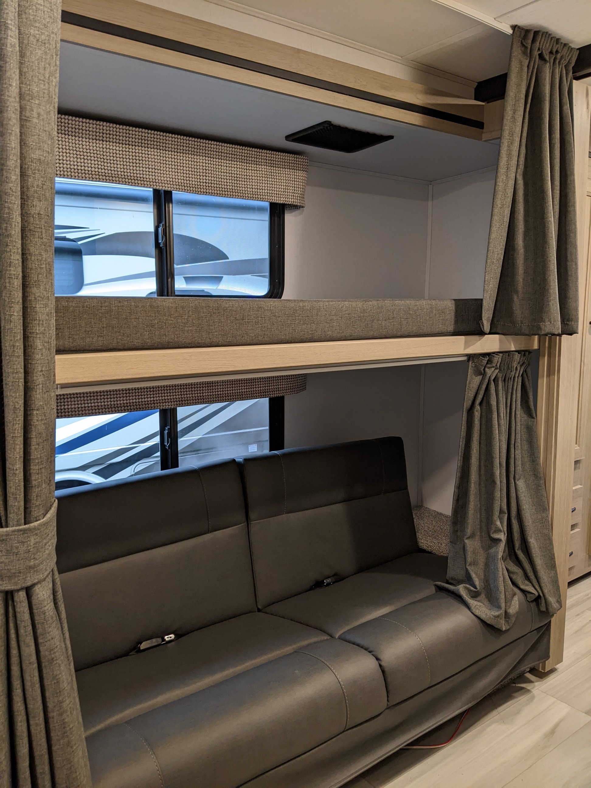 Exploring an RV rental: A modern bunk bed setup with a dark grey convertible sofa, privacy curtains, and windows.. Forest River Sunseeker 2025