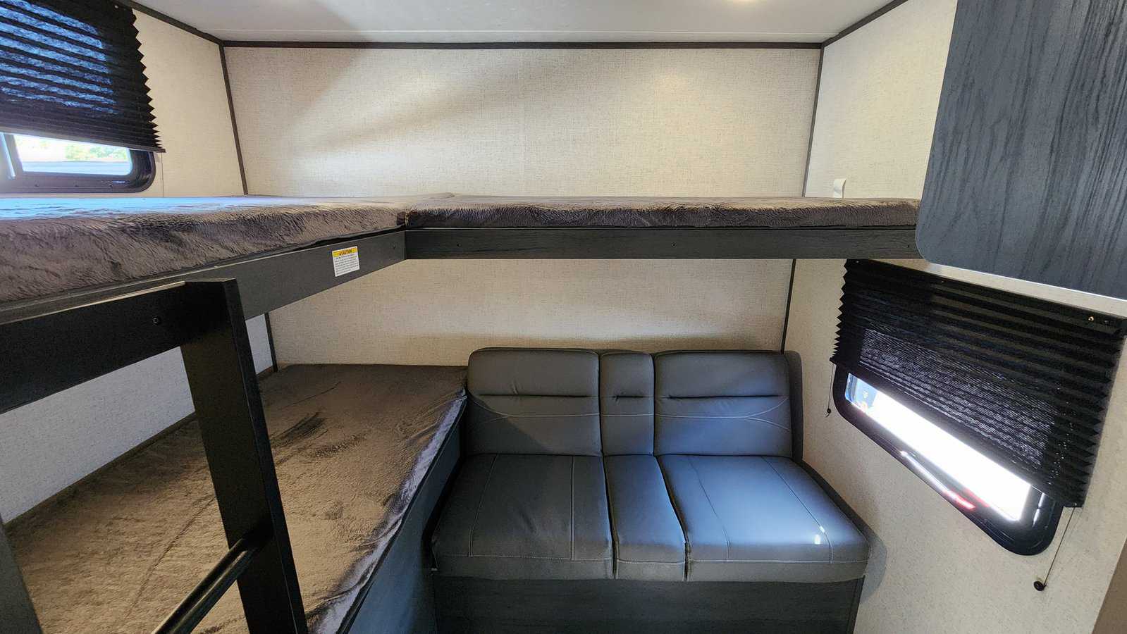 RV rental interior showing dark grey bunk beds (two levels) and a matching sofa. Black window blinds add privacy for travel.. Aspen Trail LE 2023