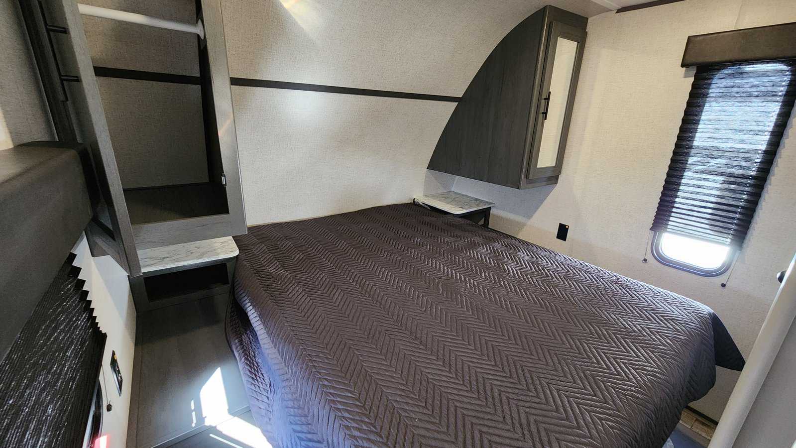 Modern RV rental bedroom: a comfy bed, open wardrobe, mirrored cabinet, and window for natural light await.. Aspen Trail LE 2023