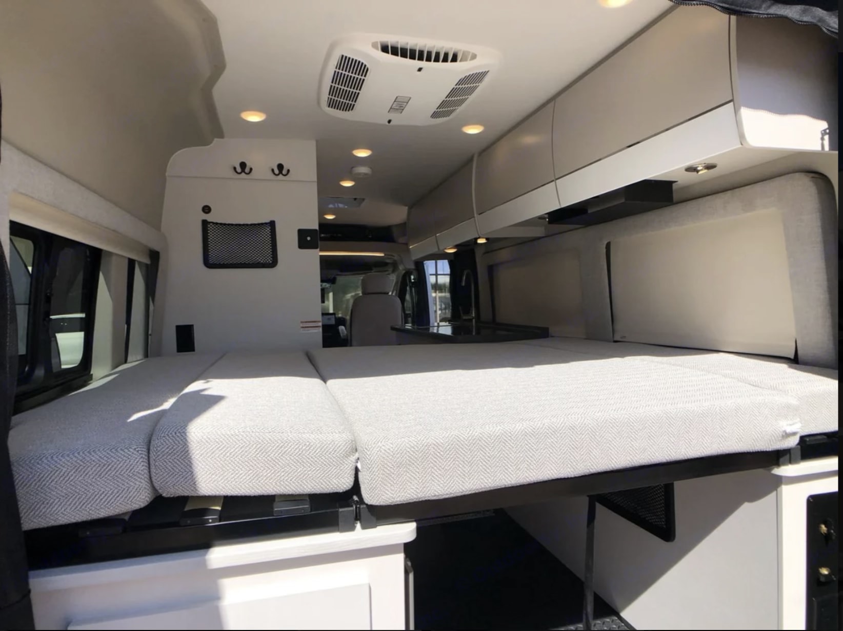 Cozy RV rental interior with a bed featuring chevron cushions, overhead cabinets, ceiling lights, and an AC unit.. Entegra Coach Ethos 2025