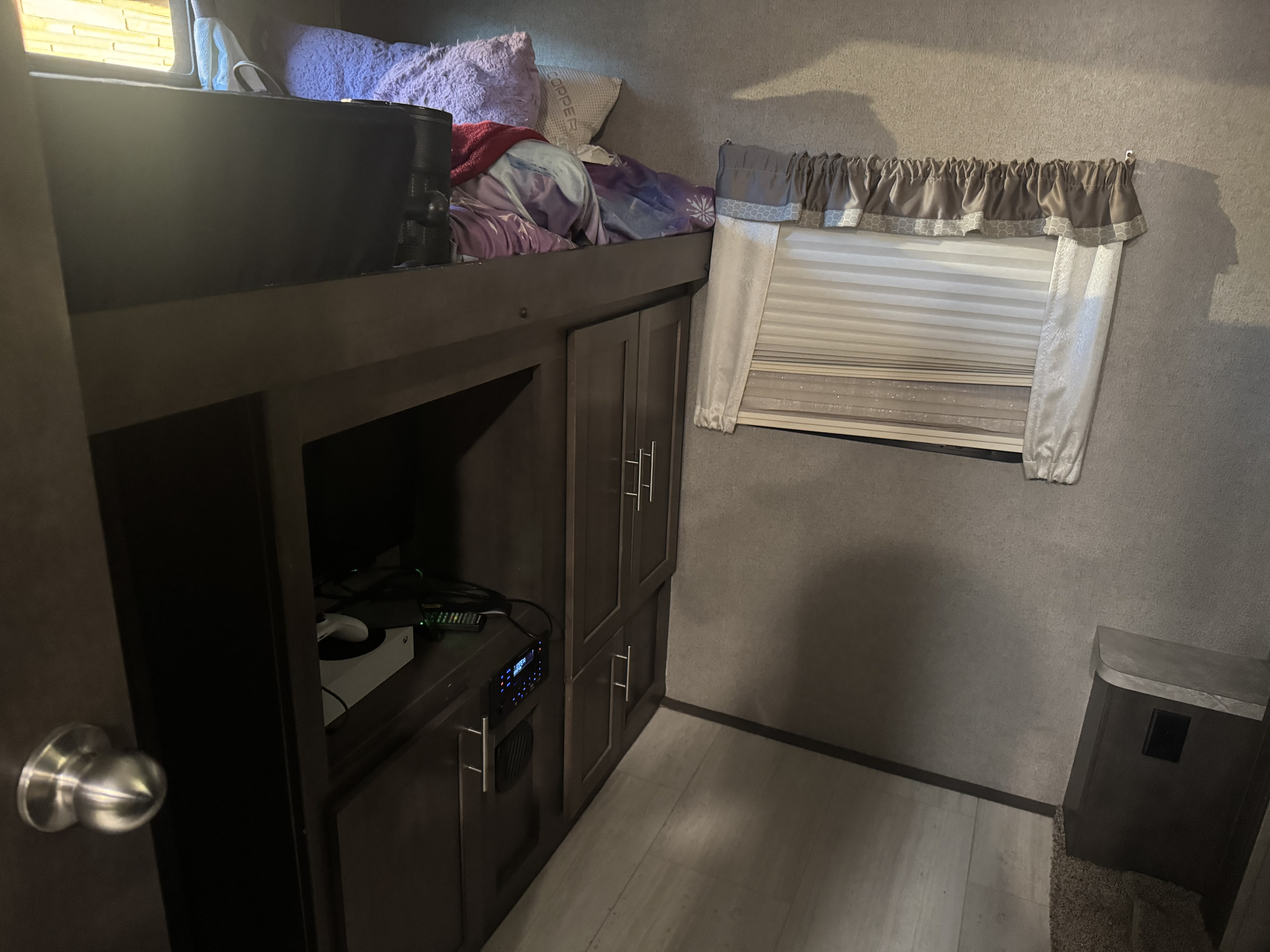 An RV rental's compact living space: bunk bed, entertainment center with game console, and window with blinds.. Forest River Flagstaff Classic 2020