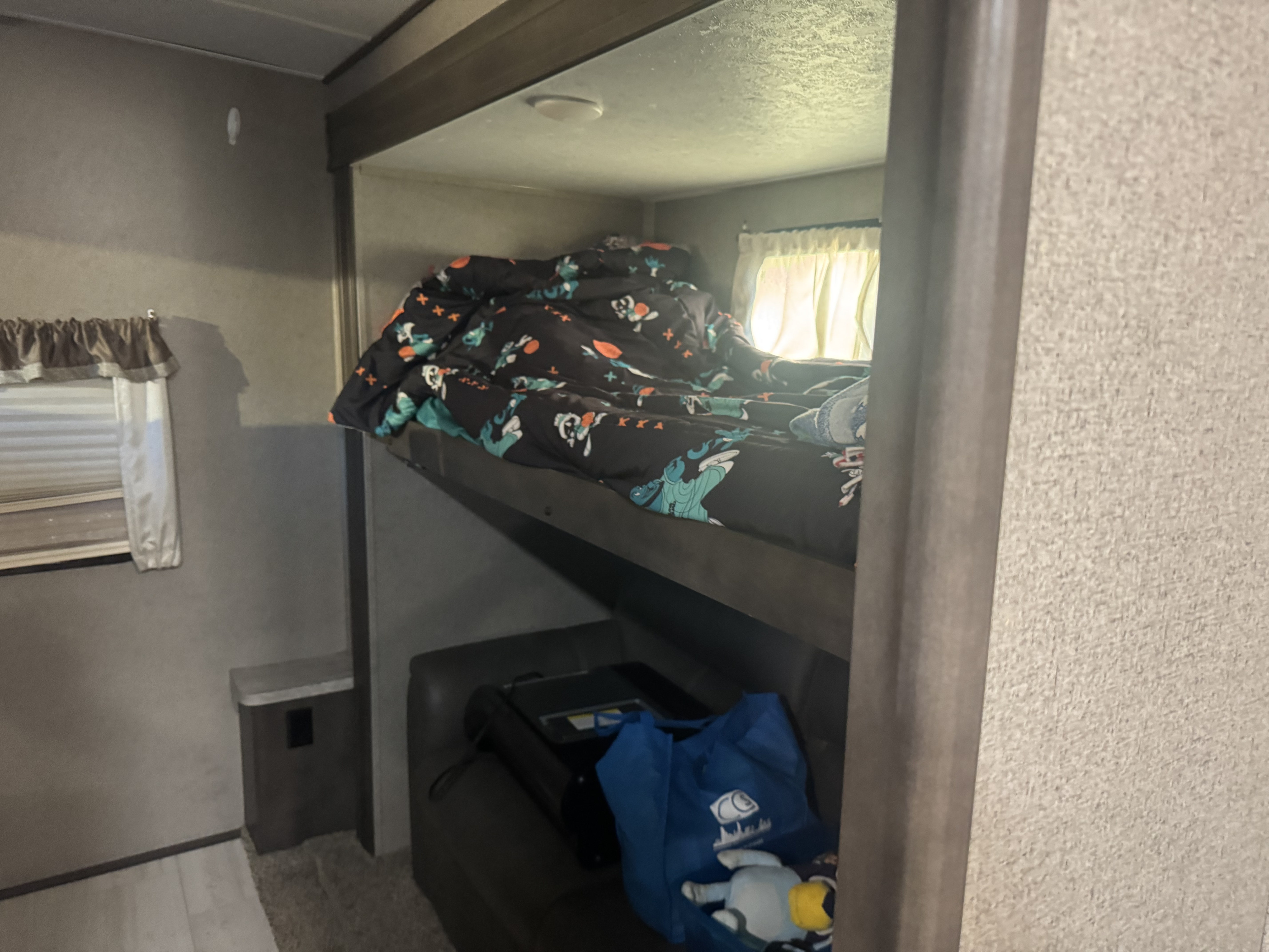 RV rental interior: a view of bunk beds. The upper bunk has a patterned duvet, and below is a seating area with a bag.. Forest River Flagstaff Classic 2020