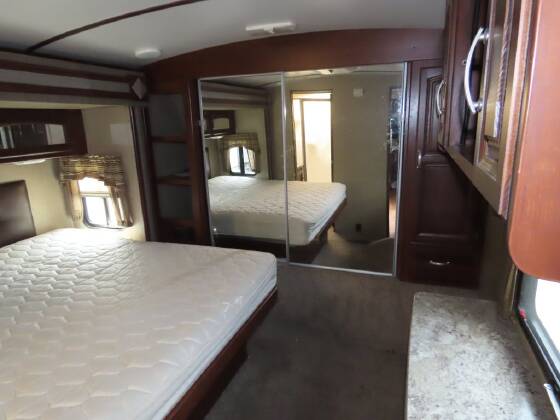 RV rental bedroom interior featuring a comfortable bed, large mirrored closet, and wood-toned cabinetry with a window.. Keystone RV Outback Super-Lite 2016