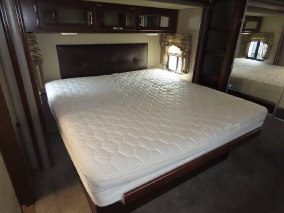 Cozy RV rental bedroom featuring a white mattress on a dark wood frame, dark headboard, and overhead cabinets for storage.. Keystone RV Outback Super-Lite 2016