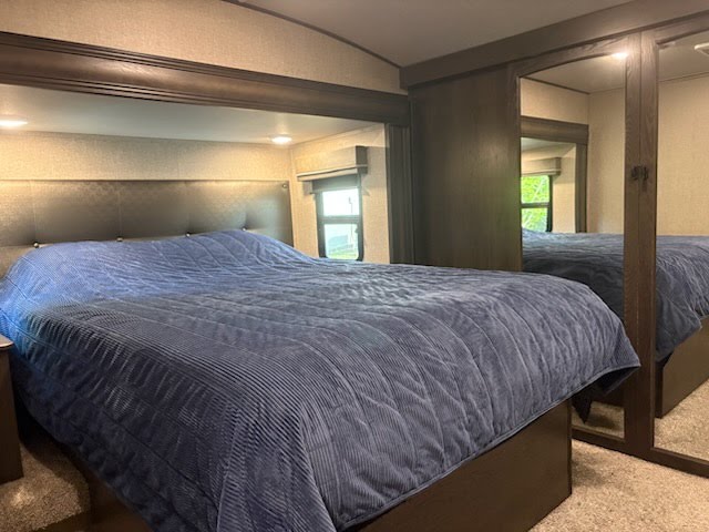 Spacious RV rental bedroom: comfy bed with a quilted blue comforter & mirrored closet doors, offering a relaxing travel stay.. Grand Design Reflection 2023