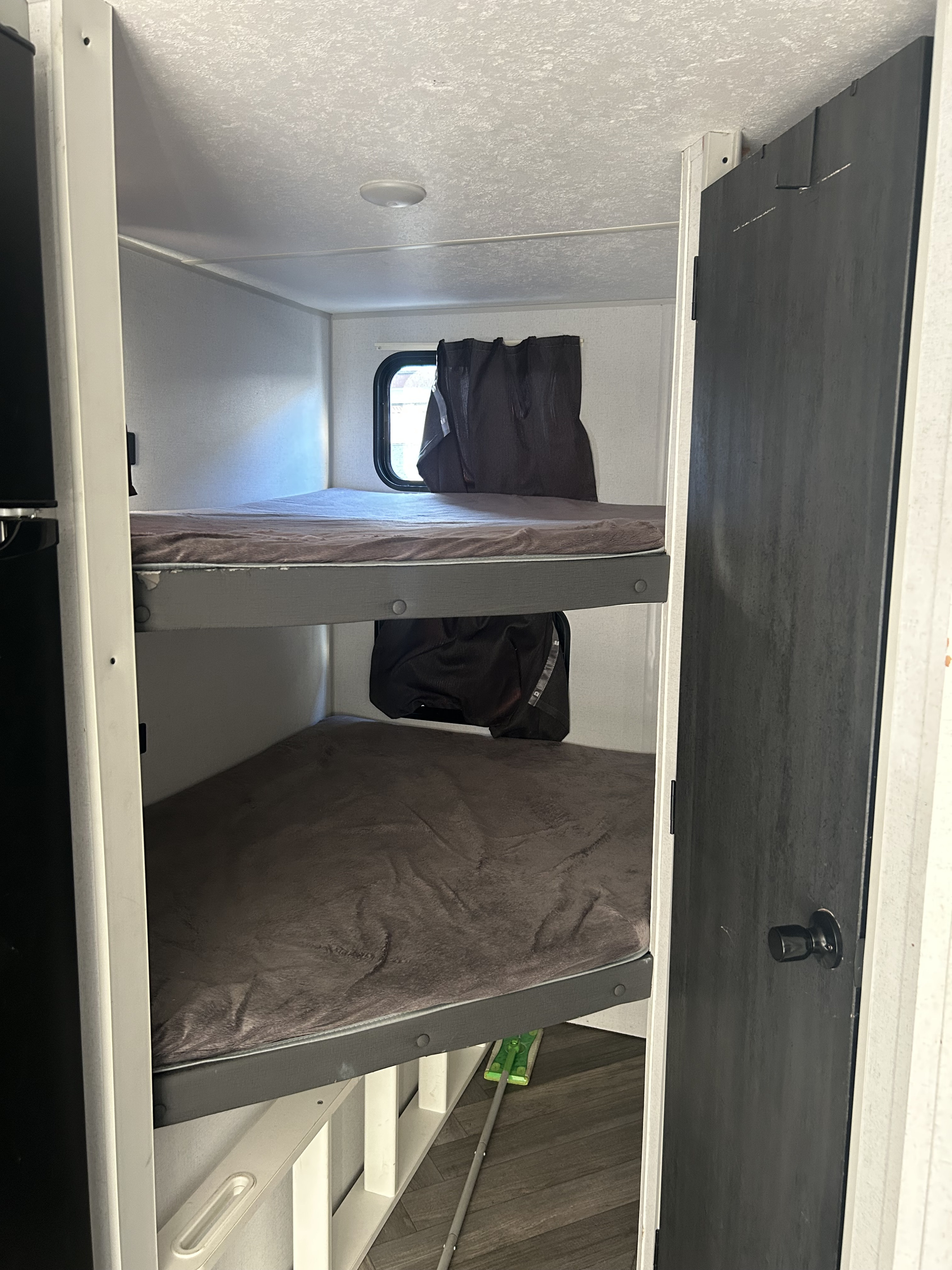 Inside an RV rental: two bunk beds with brown bedding, a window with curtains, and a dark interior door, offering compact sleeping.. Forest River Salem FSX 2021