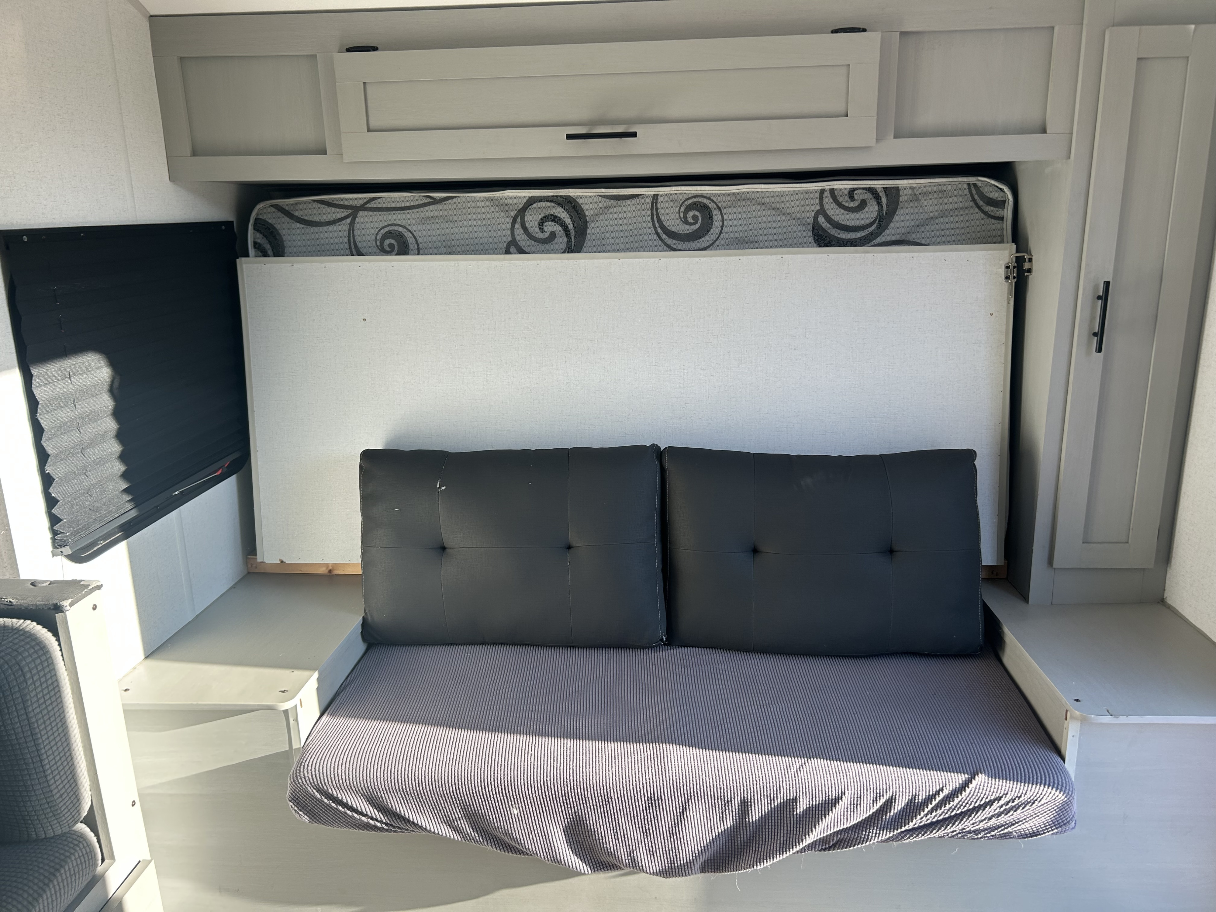 Compact RV rental interior with a gray sofa that converts to a bed, mattress stored above, and light overhead cabinets.. Forest River Salem FSX 2021
