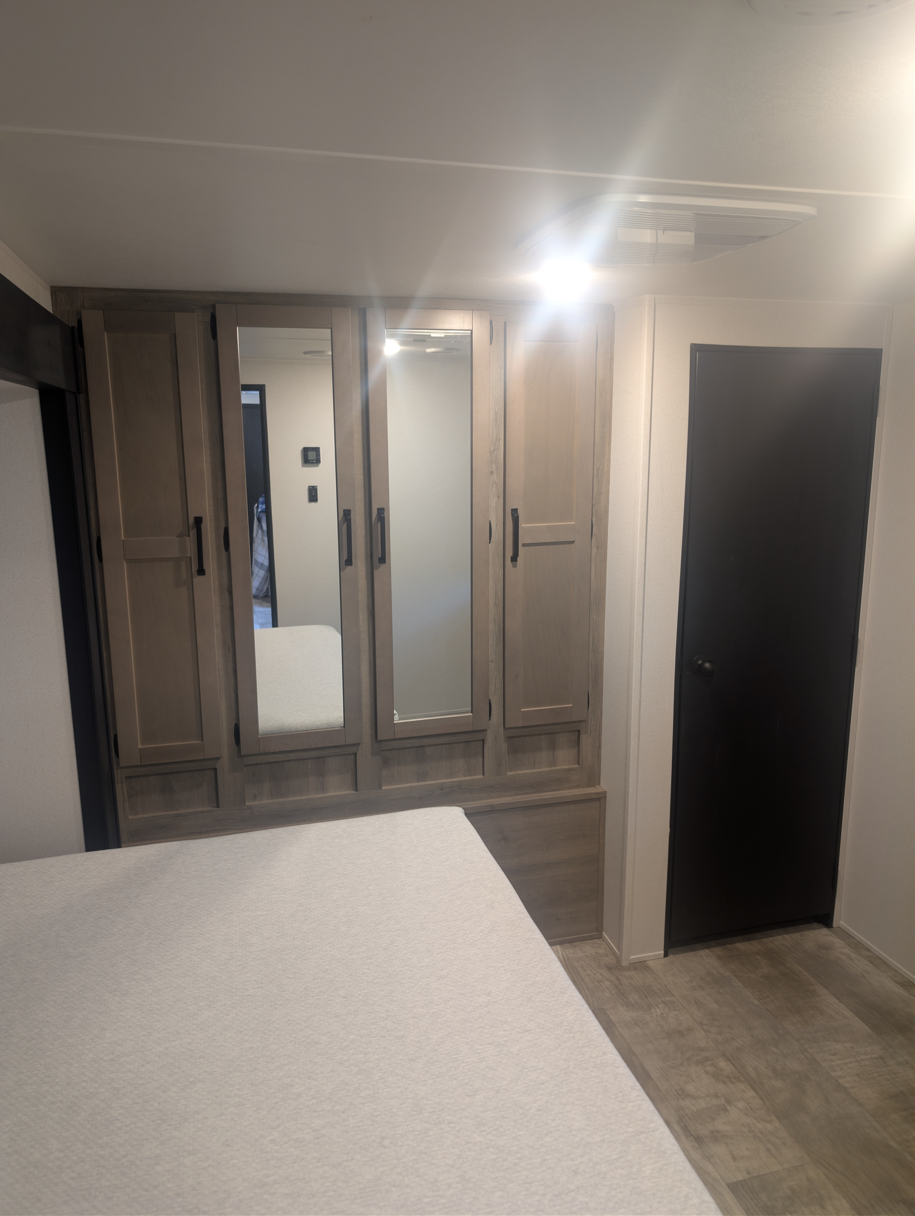 Modern RV rental bedroom interior with light wood cabinets, mirrored doors, comfortable bed, and a dark access door.. Forest River Palomino Puma 2025