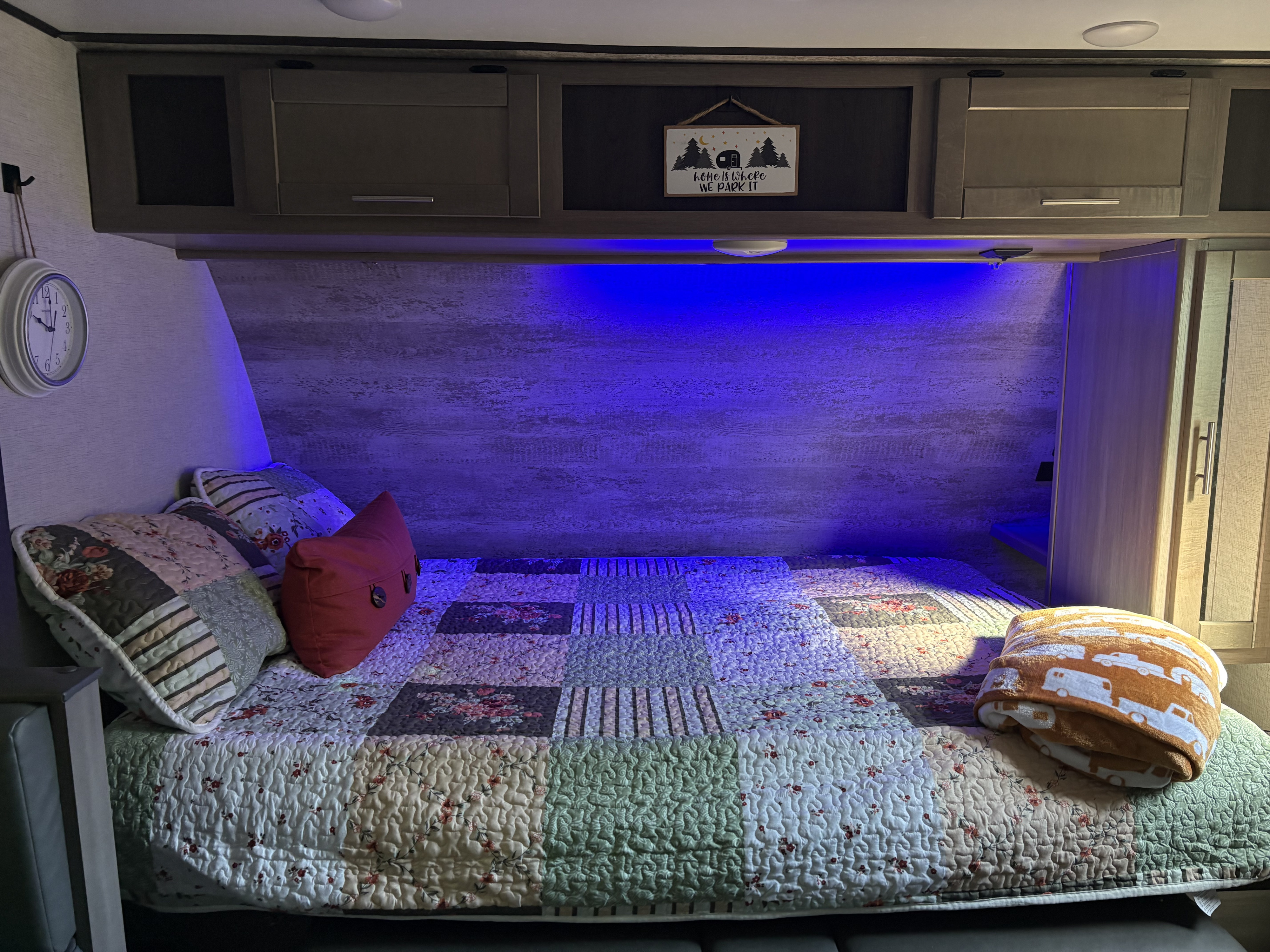 This cozy RV rental interior features a patchwork bed, blue lighting, and a "home is where we park it" sign.. Crossroads RV Sunset Trail Super Lite 2021