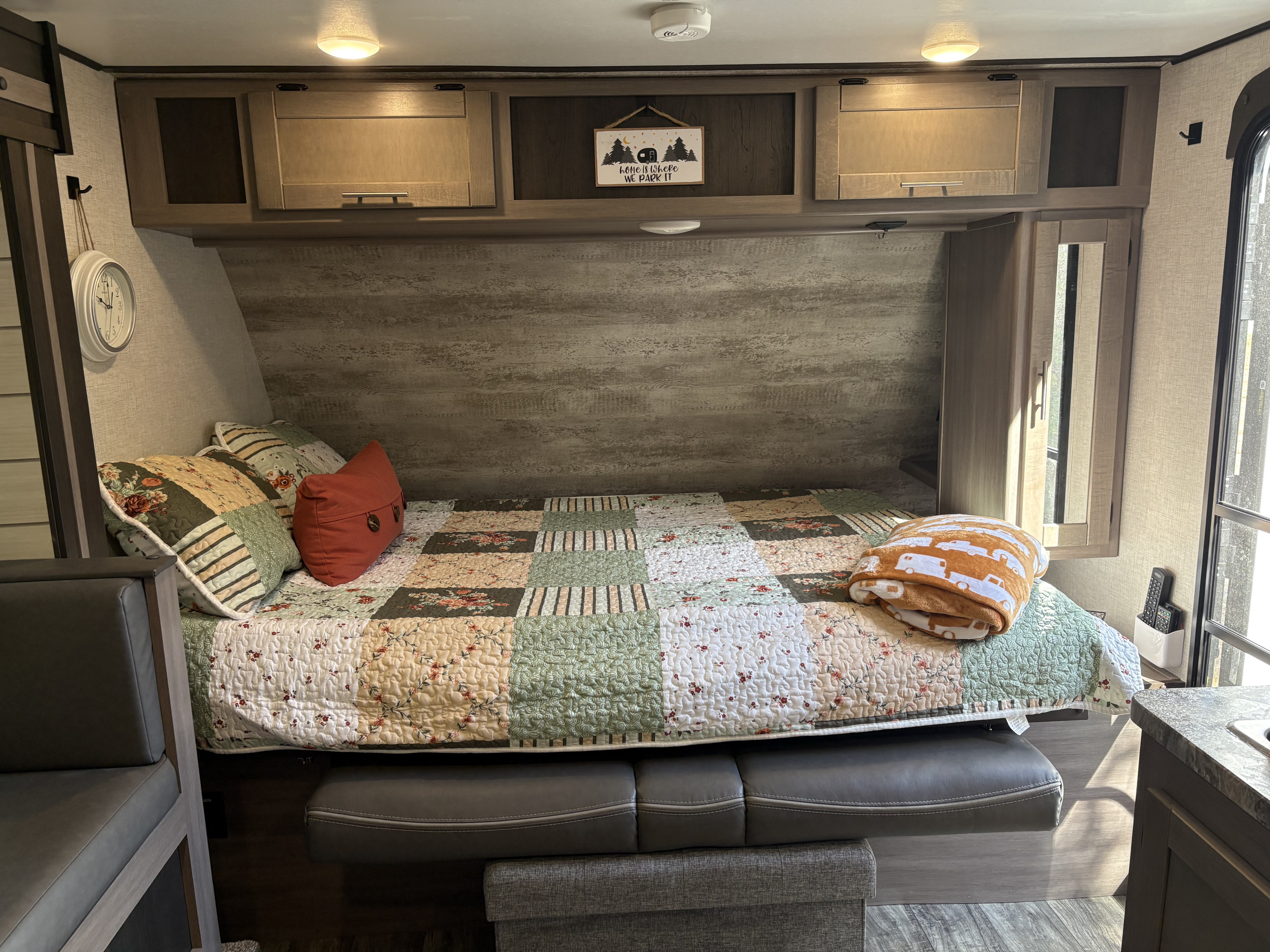 Cozy RV rental bedroom with a quilted bed, comfy pillows, overhead cabinets, and a sweet "home is where we park it" sign.. Crossroads RV Sunset Trail Super Lite 2021