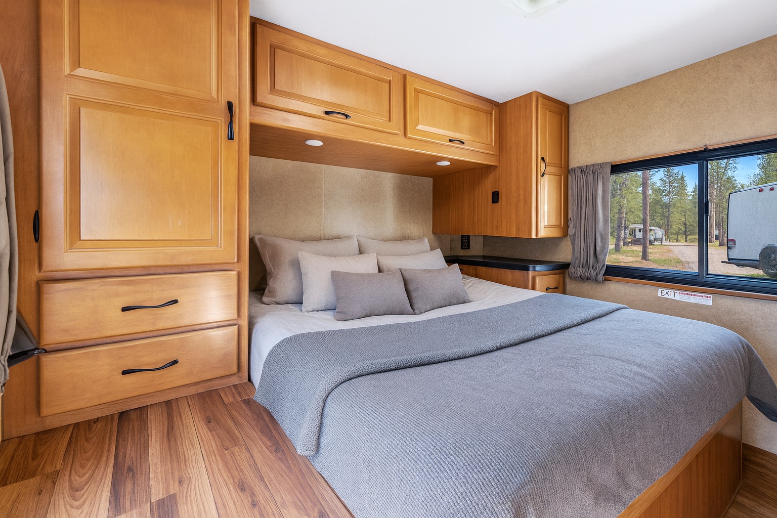 Cozy RV rental bedroom featuring ample wooden storage, a comfortable bed, and a window with a scenic view of a campsite.. Thor Majestic 2015