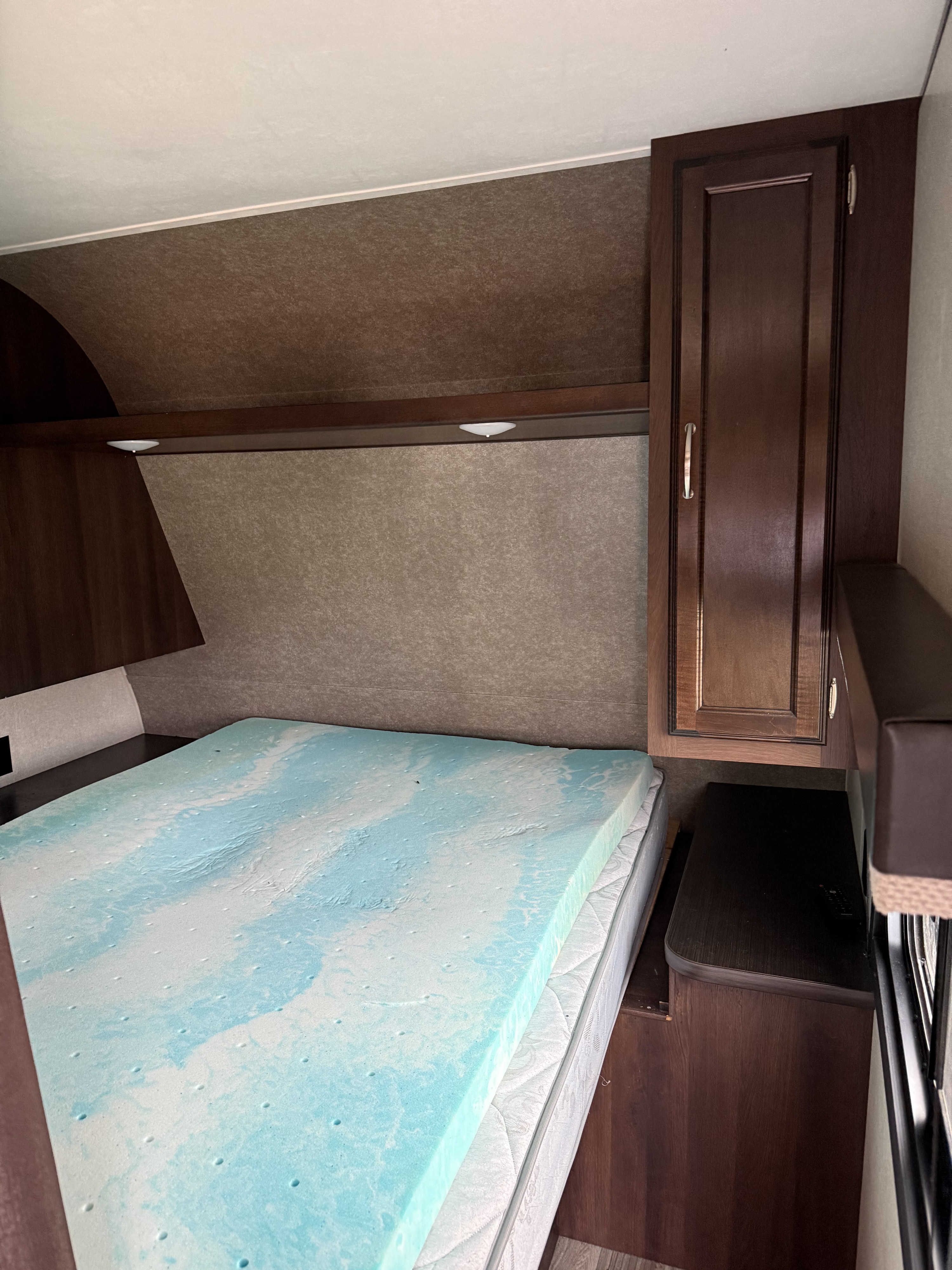 RV rental interior: A bed with a blue memory foam topper, dark wood cabinets, and overhead lights for a cozy sleeping area.. Jayco Jay Flight 2018