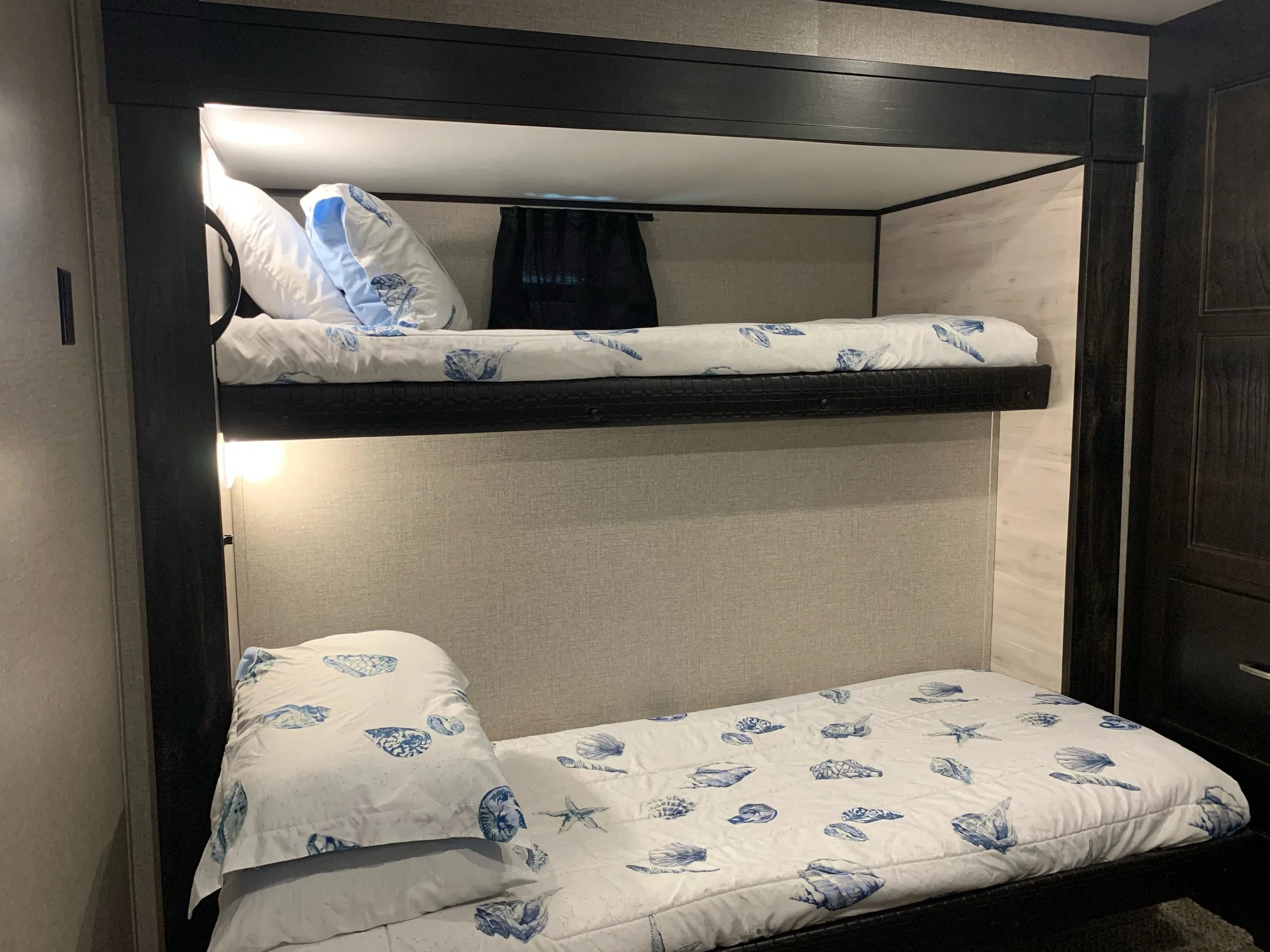 RV rental bunk beds: white and blue seashell bedding, dark wood frame, and integrated lighting for cozy sleeping. Great for families.. Jayco Jay Feather 2020