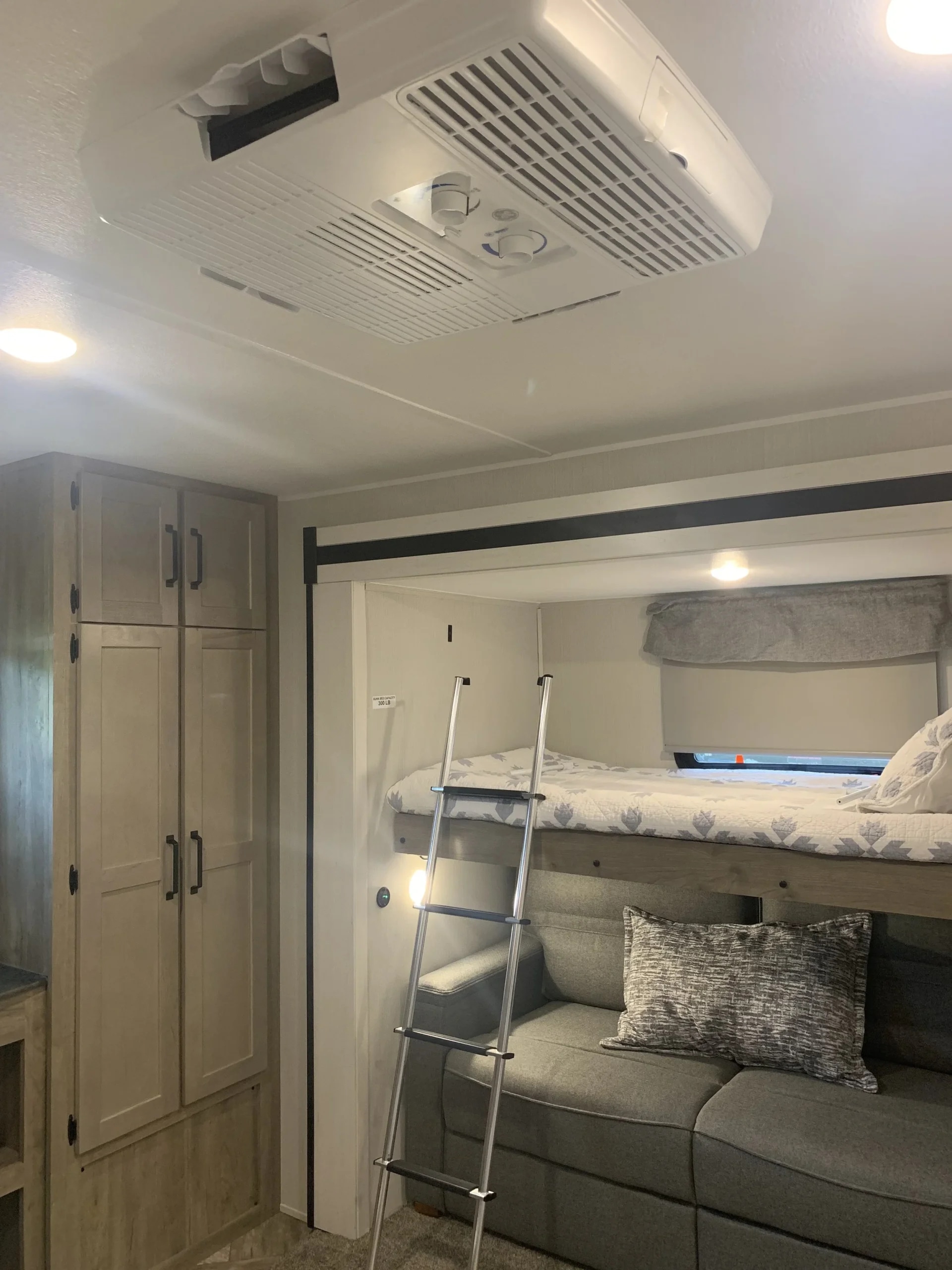 Cozy RV rental interior with bunk beds, ladder, gray sofa, and ceiling air conditioning unit for comfortable travel.. Forest River Puma 2023