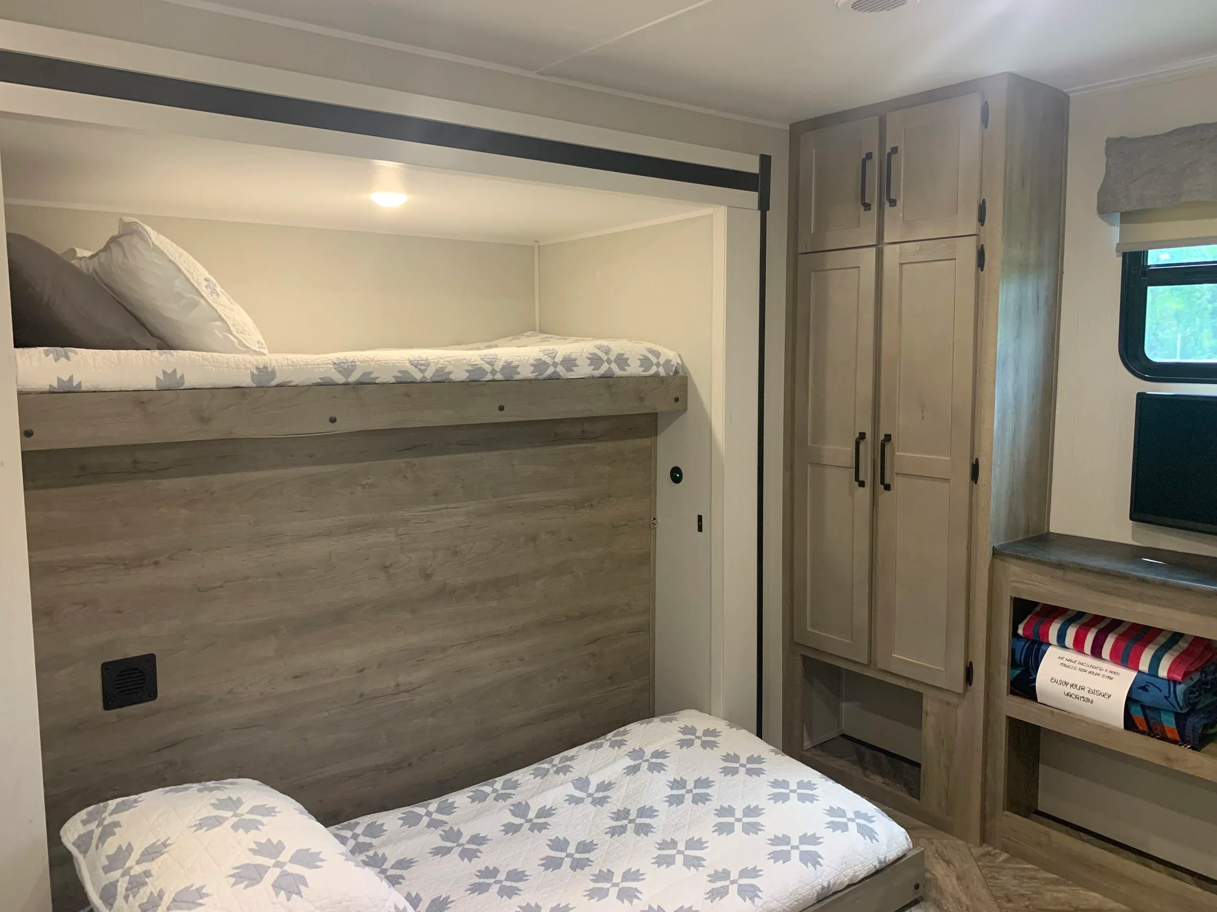 Cozy RV rental interior featuring comfortable bunk beds with quilts, a wardrobe, and shelving with pool towels. A perfect family setup.. Forest River Puma 2023