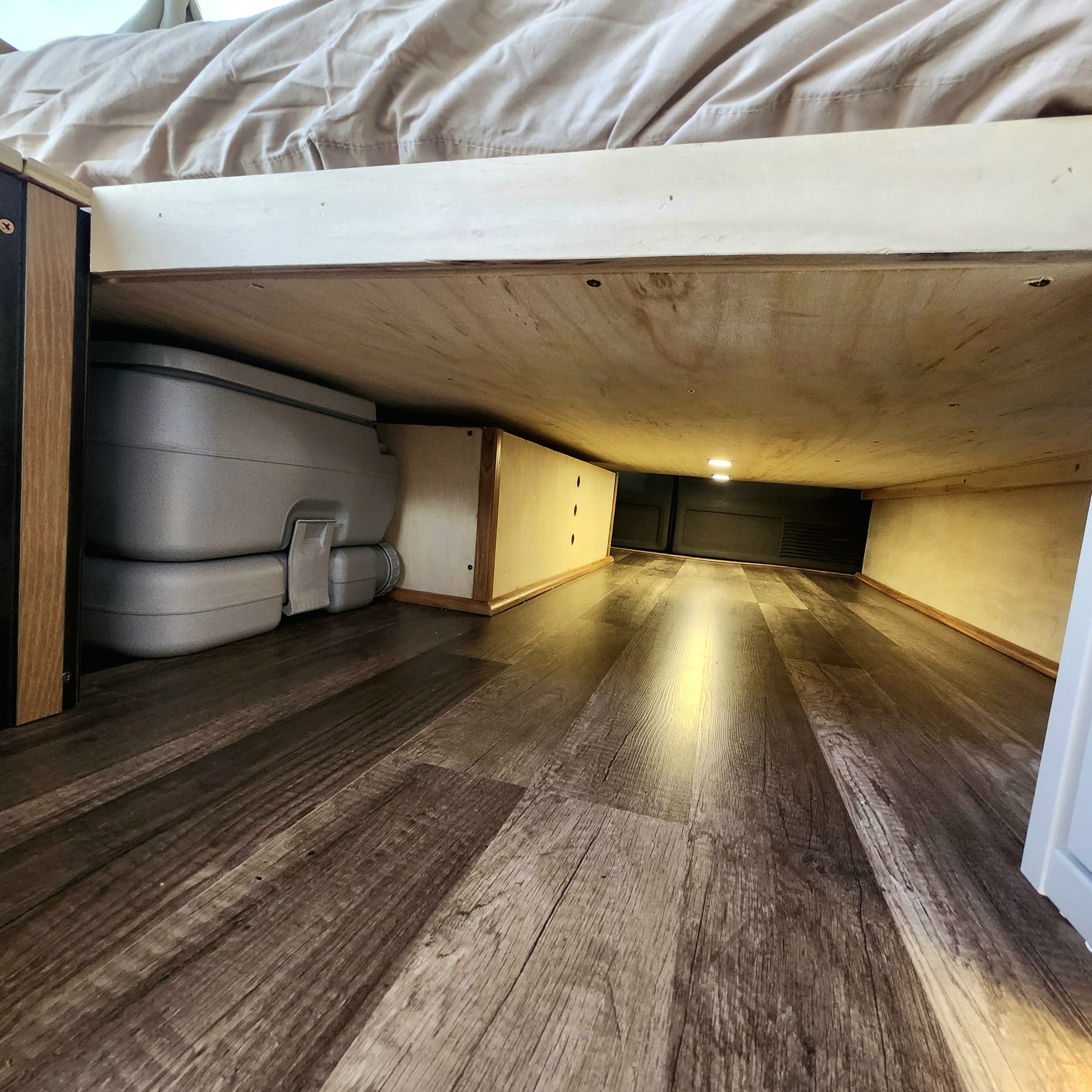 Efficient under-bed storage in this RV rental, featuring a portable toilet and wood-look flooring, optimizing small spaces.. Chevy Express 3500 2014