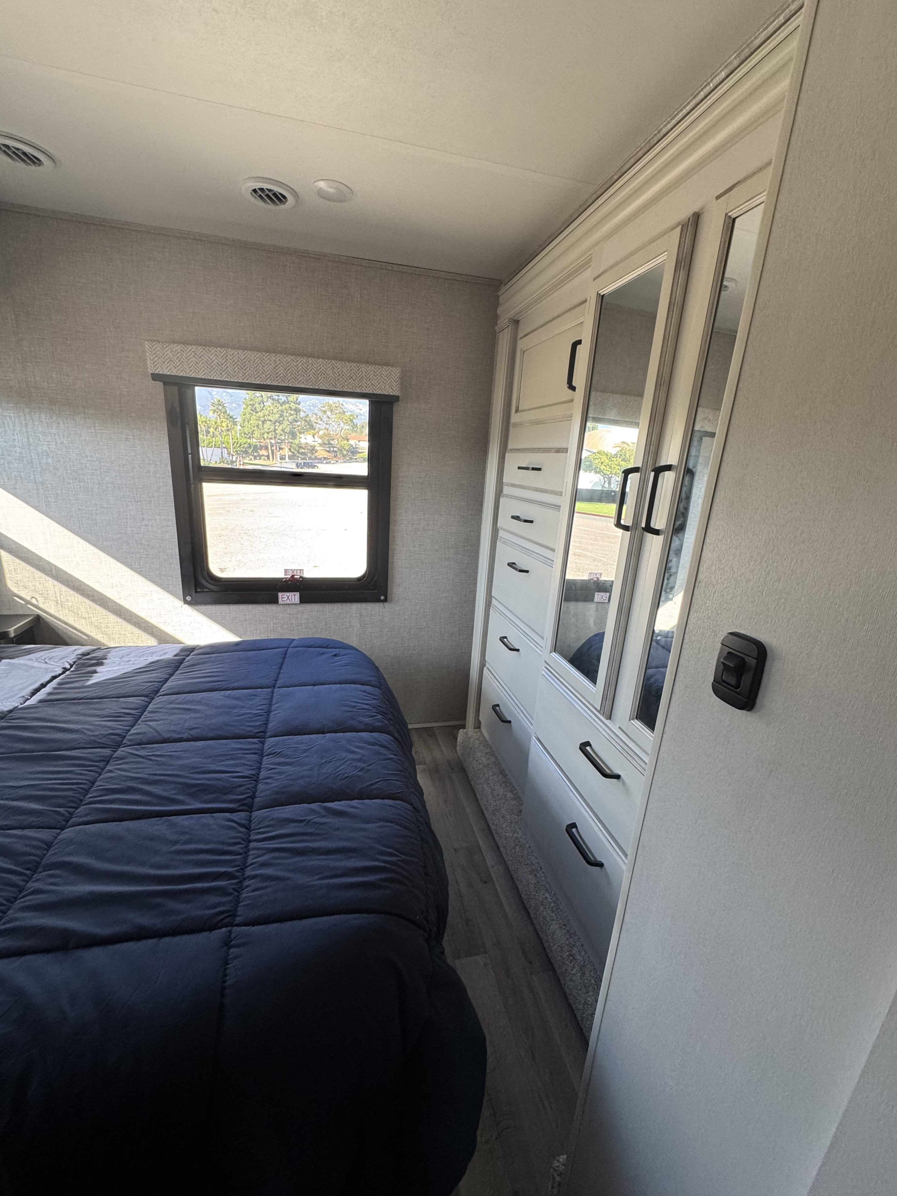 **RV rental** bedroom showing a compact bed, window with an outdoor view, and mirrored built-in wardrobe.. Jayco Redhawk 2023