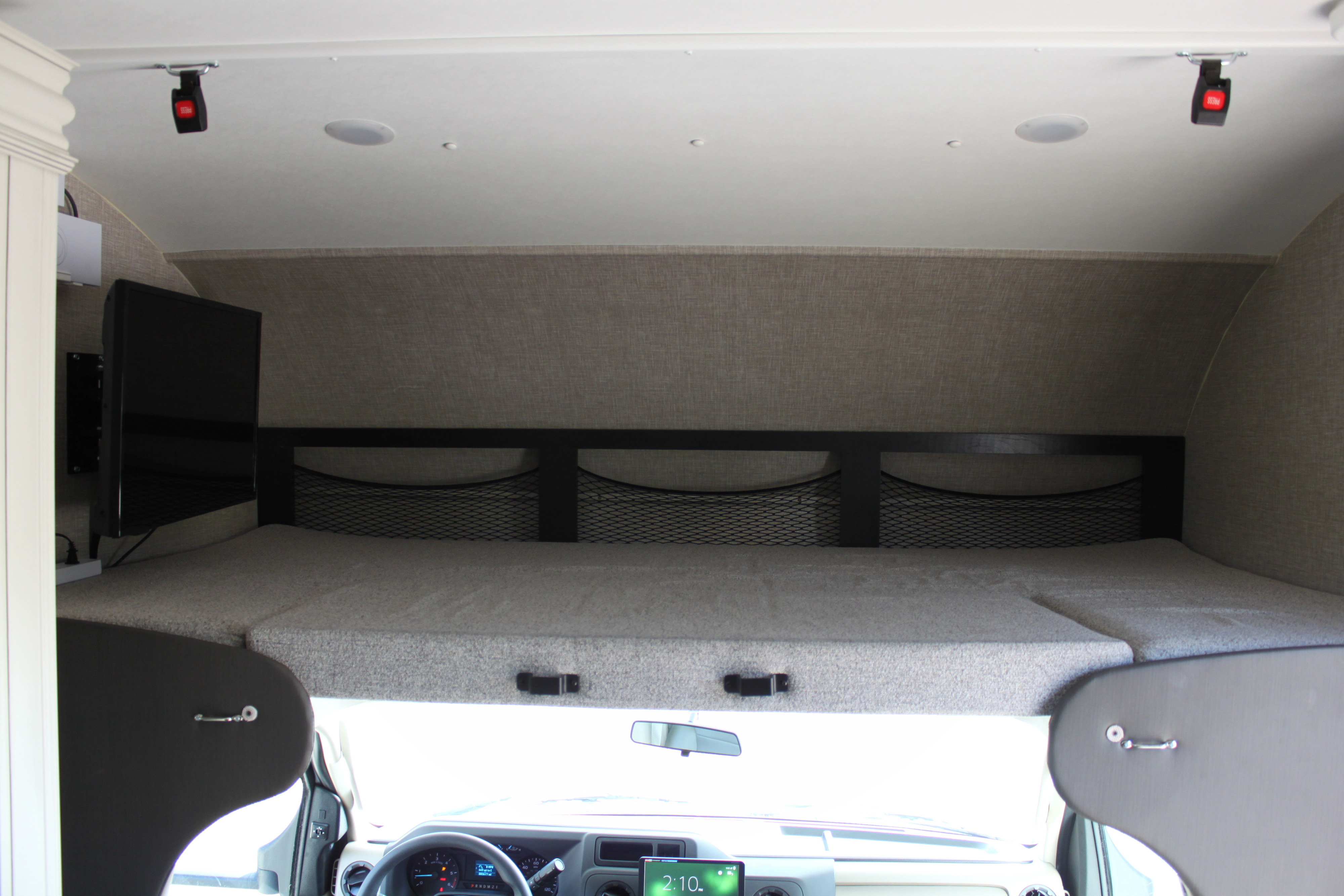 Spacious cab-over bed in an RV rental with a TV, storage nets, and safety clasps from the ceiling, offers comfy sleeping.. Jayco Redhawk 2023
